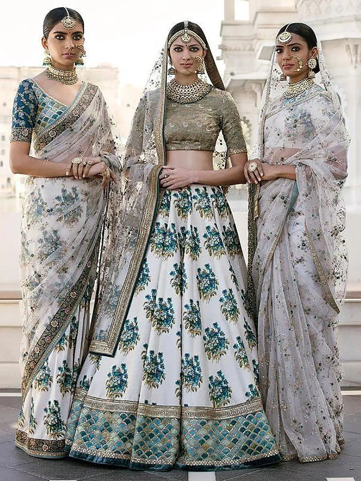 Three women in elegant Indian ethnic wear: lehenga choli and sarees with intricate embroidery and jewelry