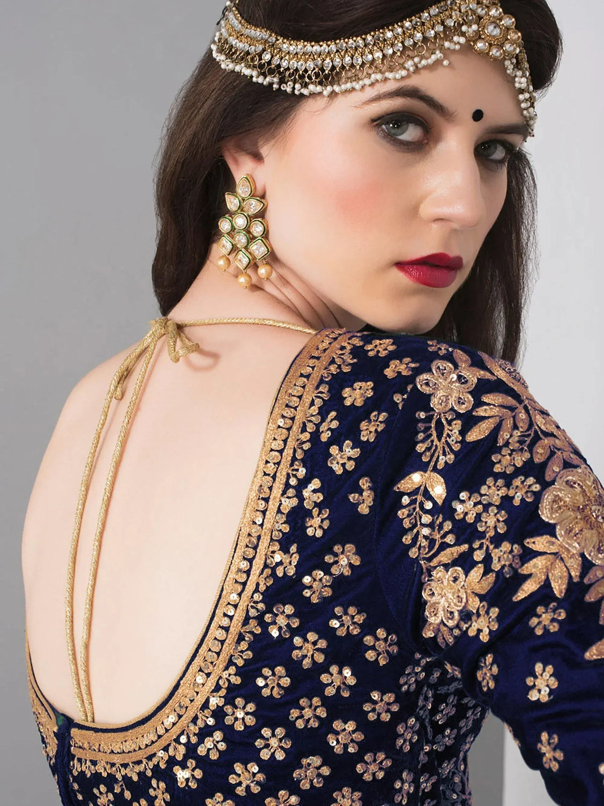 Blue velvet ethnic gown with gold floral embroidery, backless design, and traditional Indian jewelry