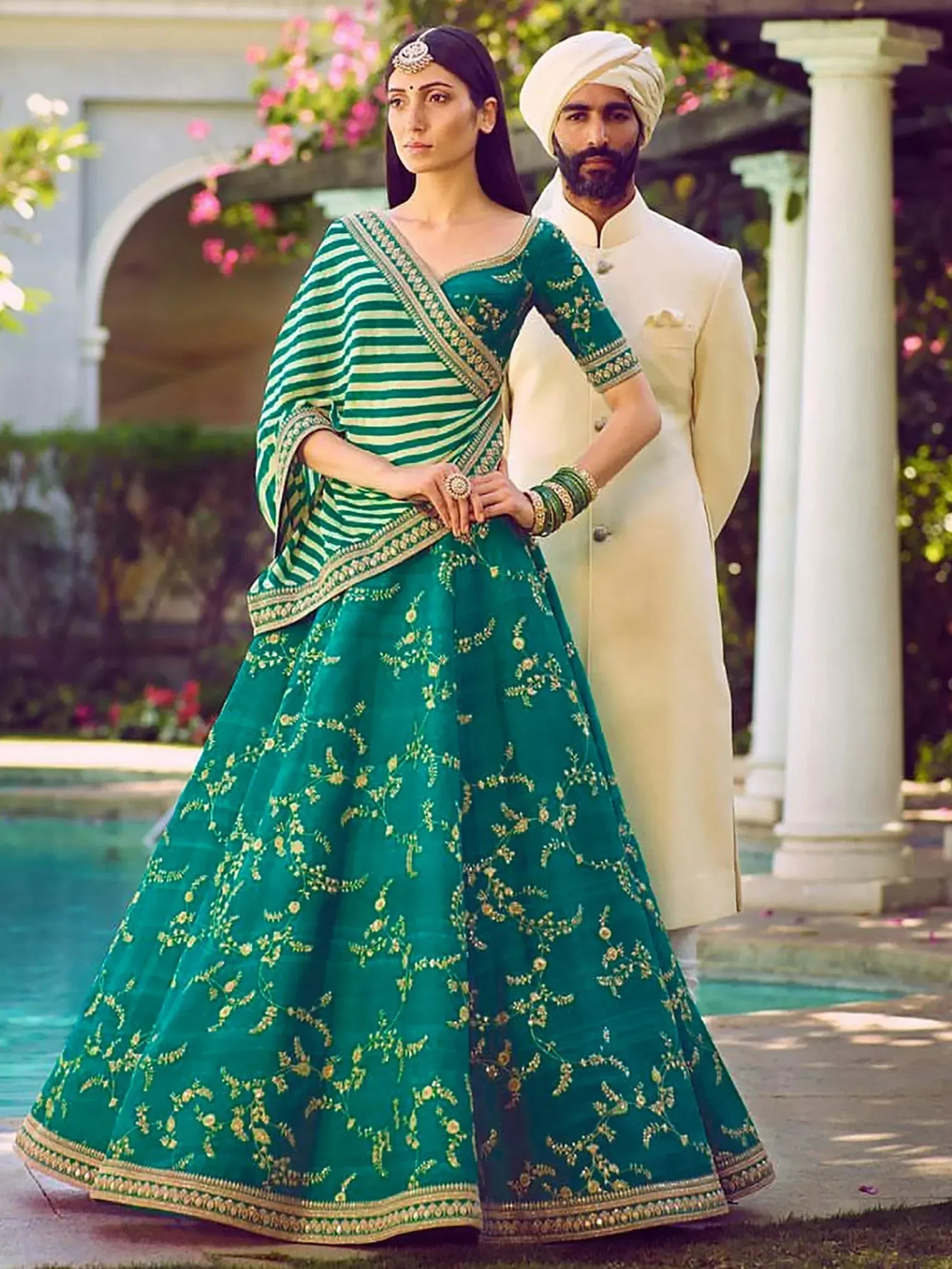 Emerald green embroidered lehenga choli with striped dupatta, paired with cream sherwani for Indian wedding