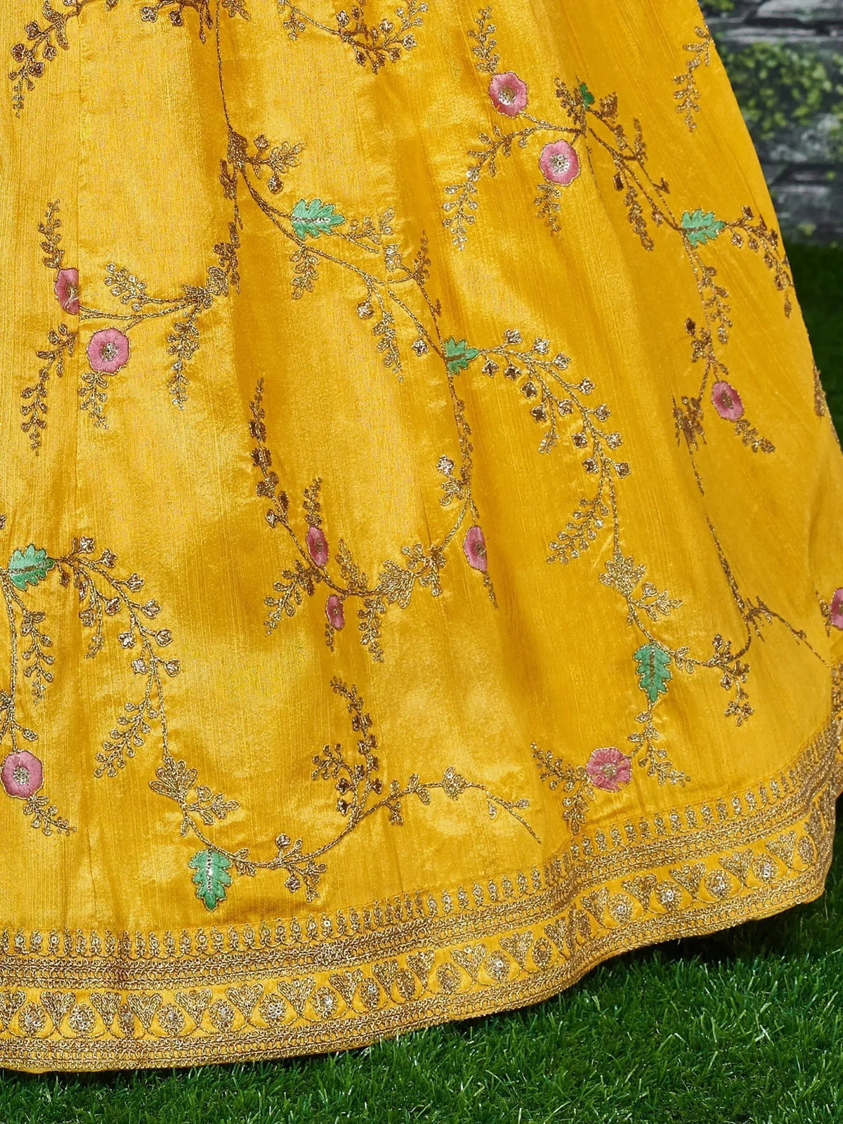 Yellow ethnic lehenga with pink floral embroidery and gold detailing on grass