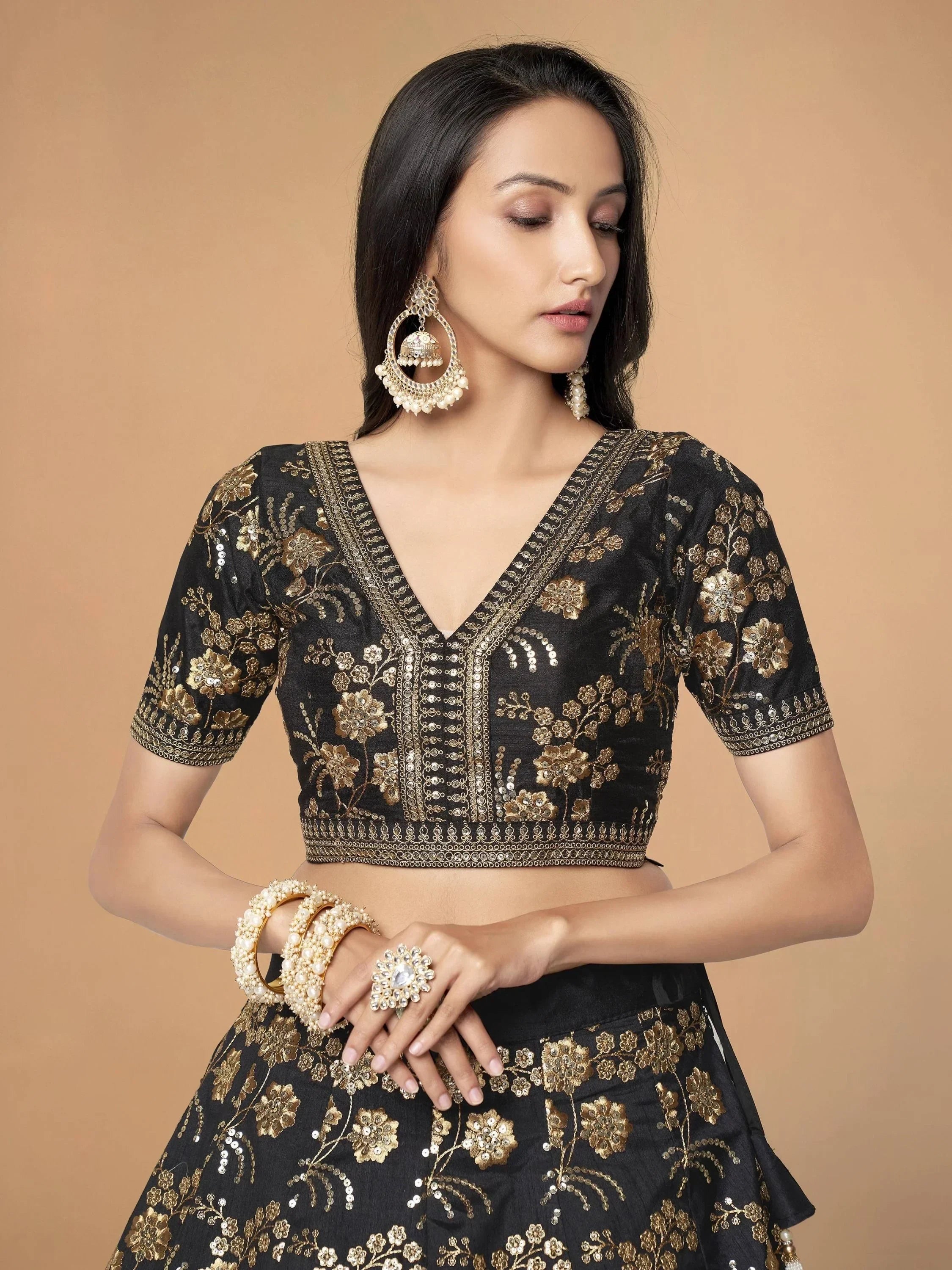 Black and gold embroidered lehenga choli with floral motifs, paired with jhumka earrings and pearl jewelry.