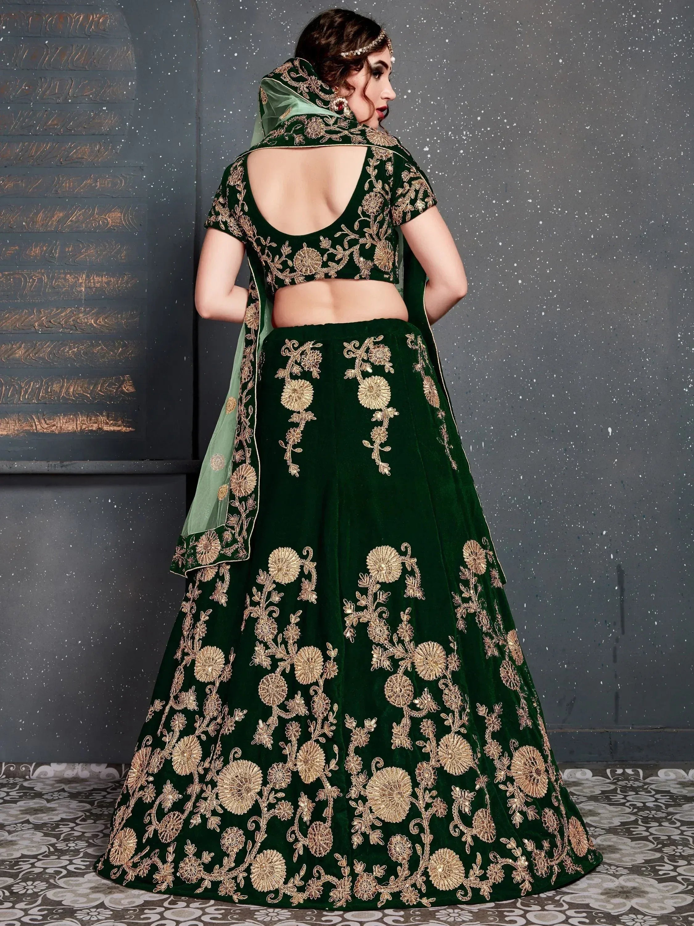 Emerald green velvet lehenga choli with gold floral embroidery and backless blouse, perfect for Indian weddings.