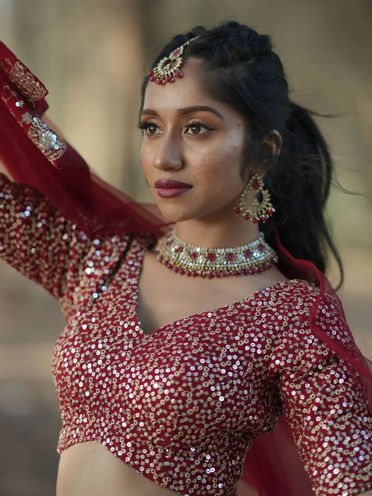 Woman in red sequin lehenga choli with gold jewelry, perfect for Indian ethnic wear occasions.