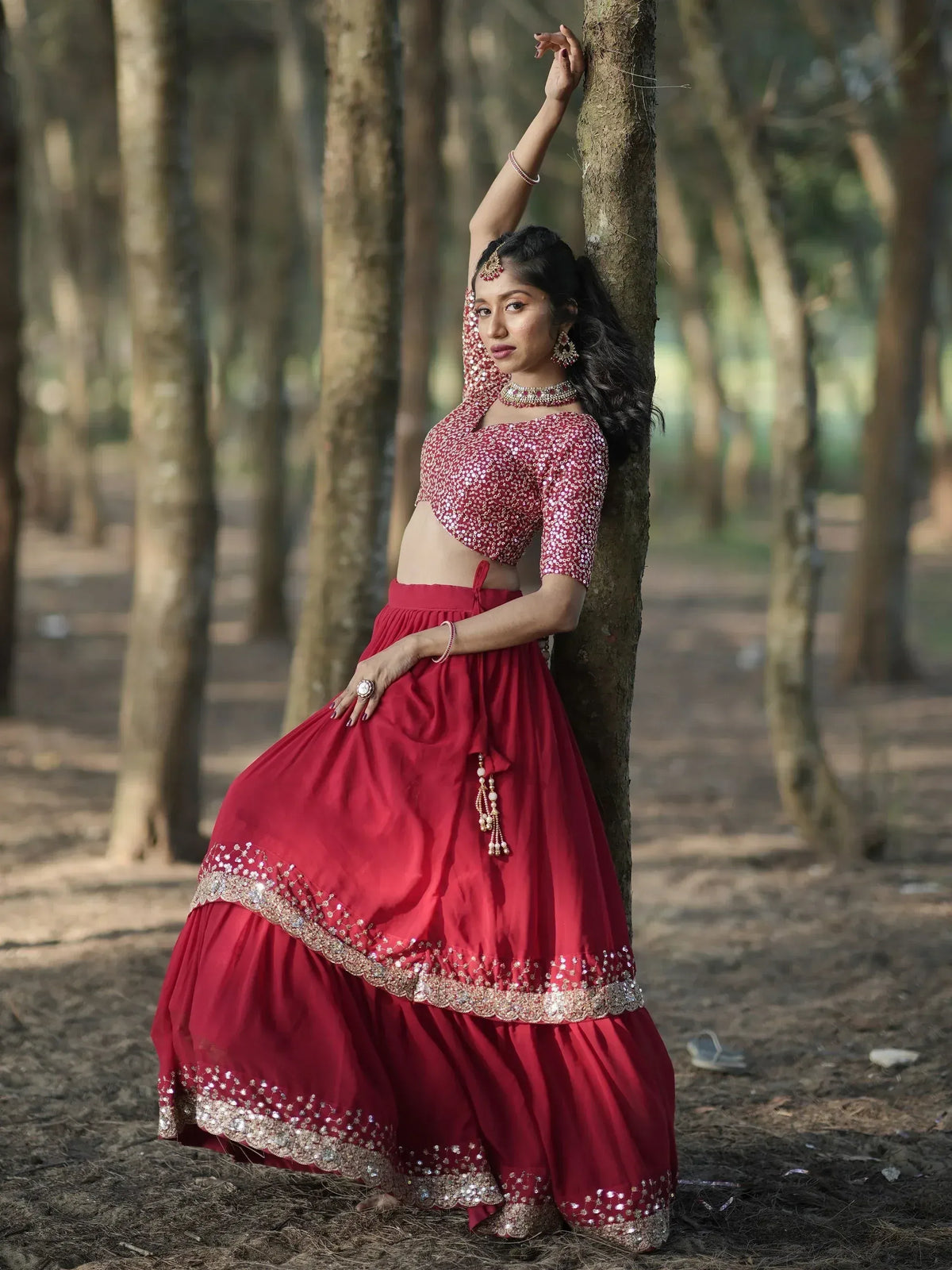 Red sequin lehenga choli with gold embroidery, worn in a forest setting