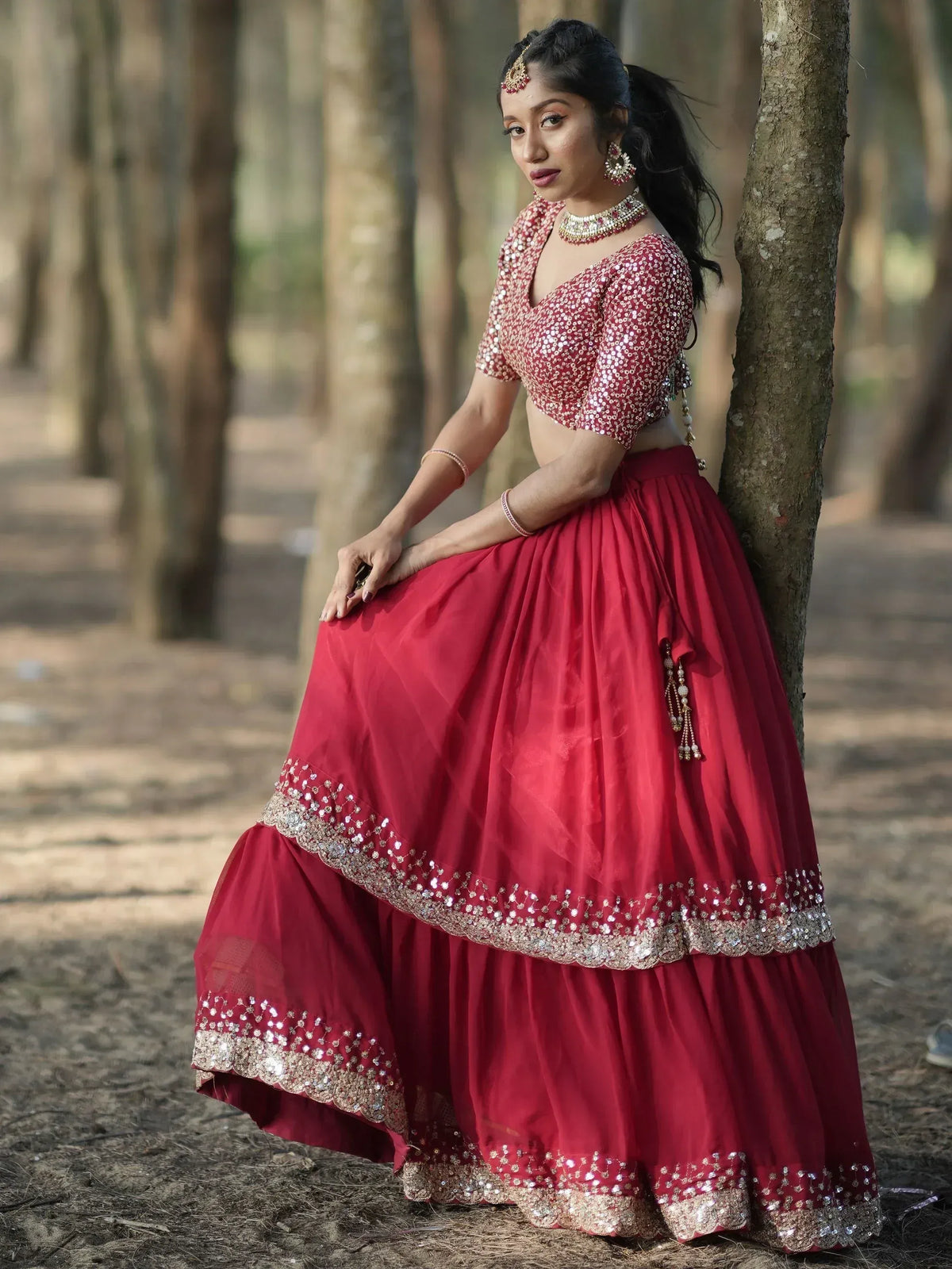 Red sequined lehenga choli with layered skirt, worn in a forest setting