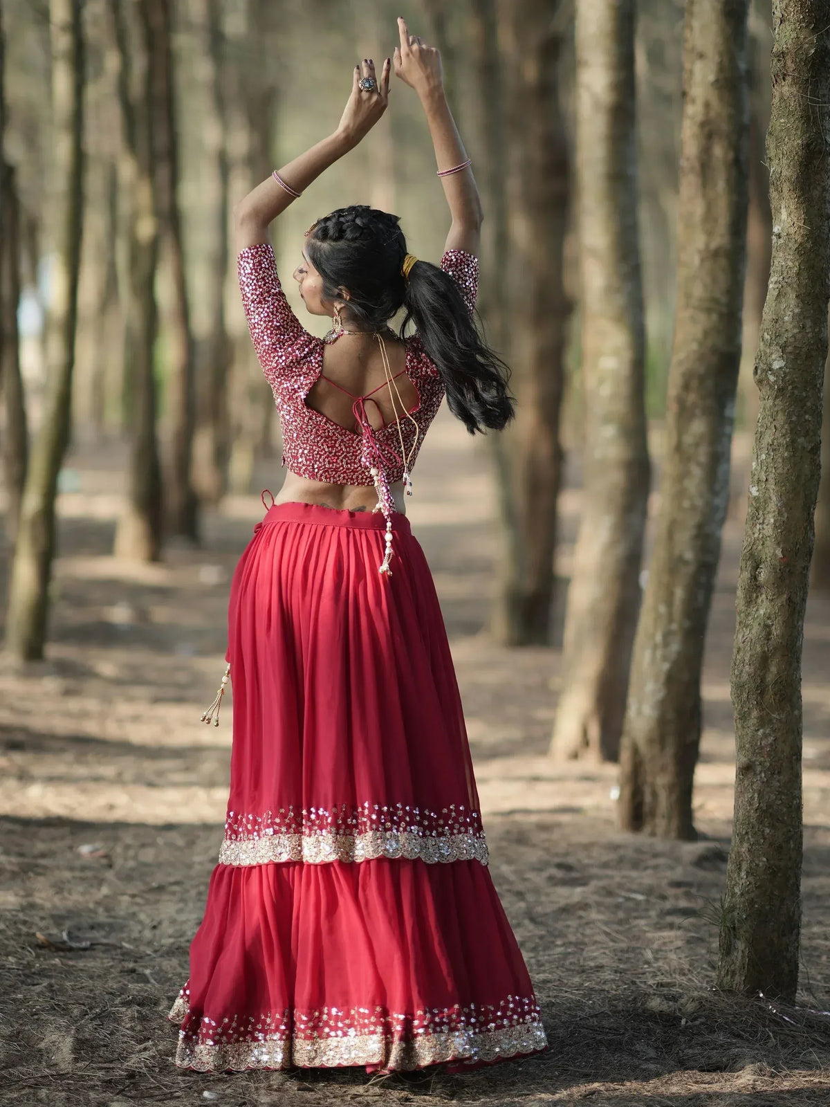 Woman in red sequin lehenga choli dancing in forest, back view with open back blouse and pleated skirt