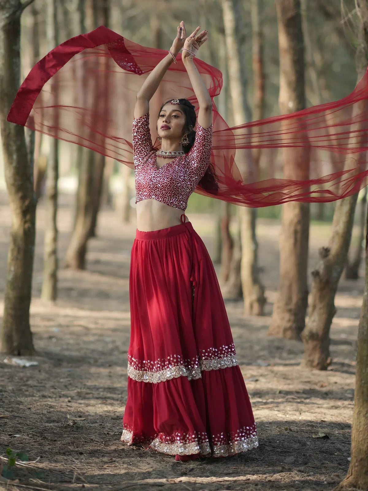 Woman in red sequined lehenga choli dancing in forest, ethnic Indian wear with flowing dupatta
