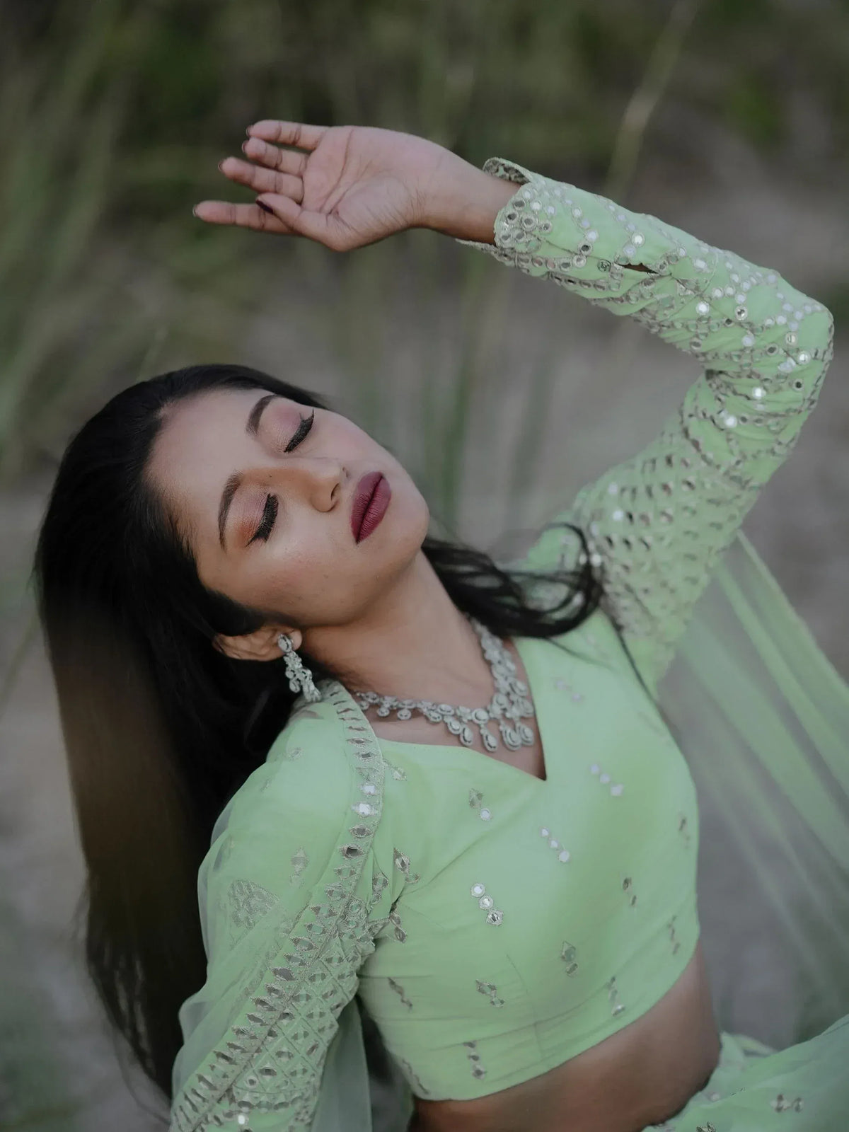 Woman in mint green ethnic lehenga choli with mirror work, posing gracefully outdoors.