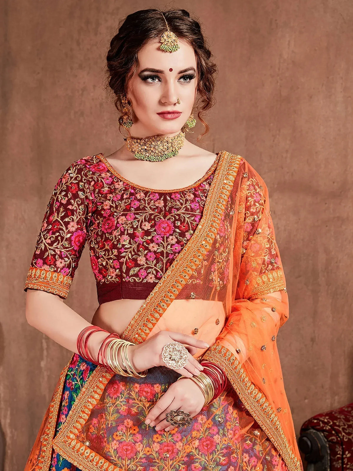 Woman in embroidered maroon and orange Indian ethnic lehenga choli with floral patterns and gold jewelry