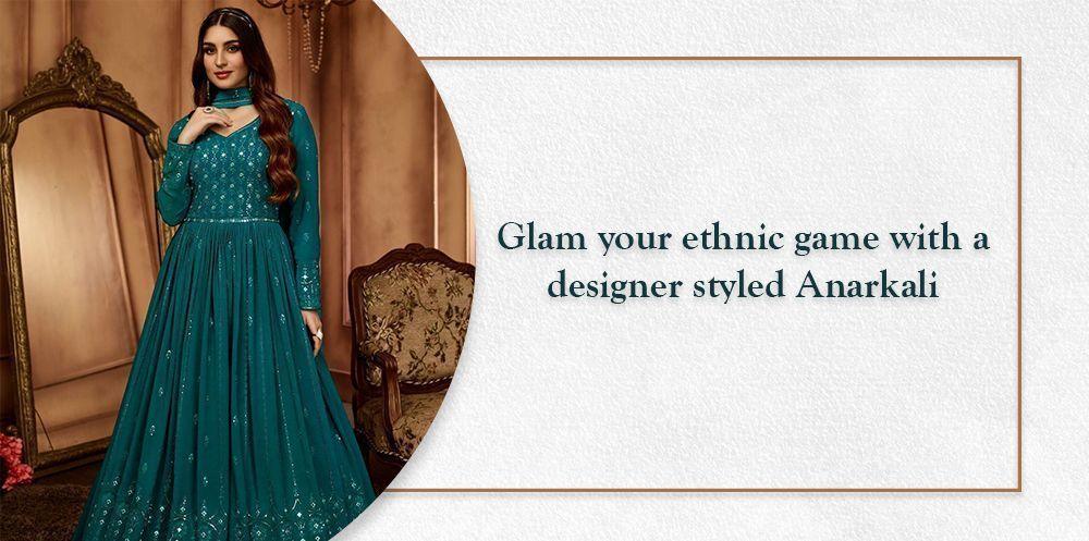 Woman in teal designer Anarkali gown with embroidery, posing in elegant ethnic setting