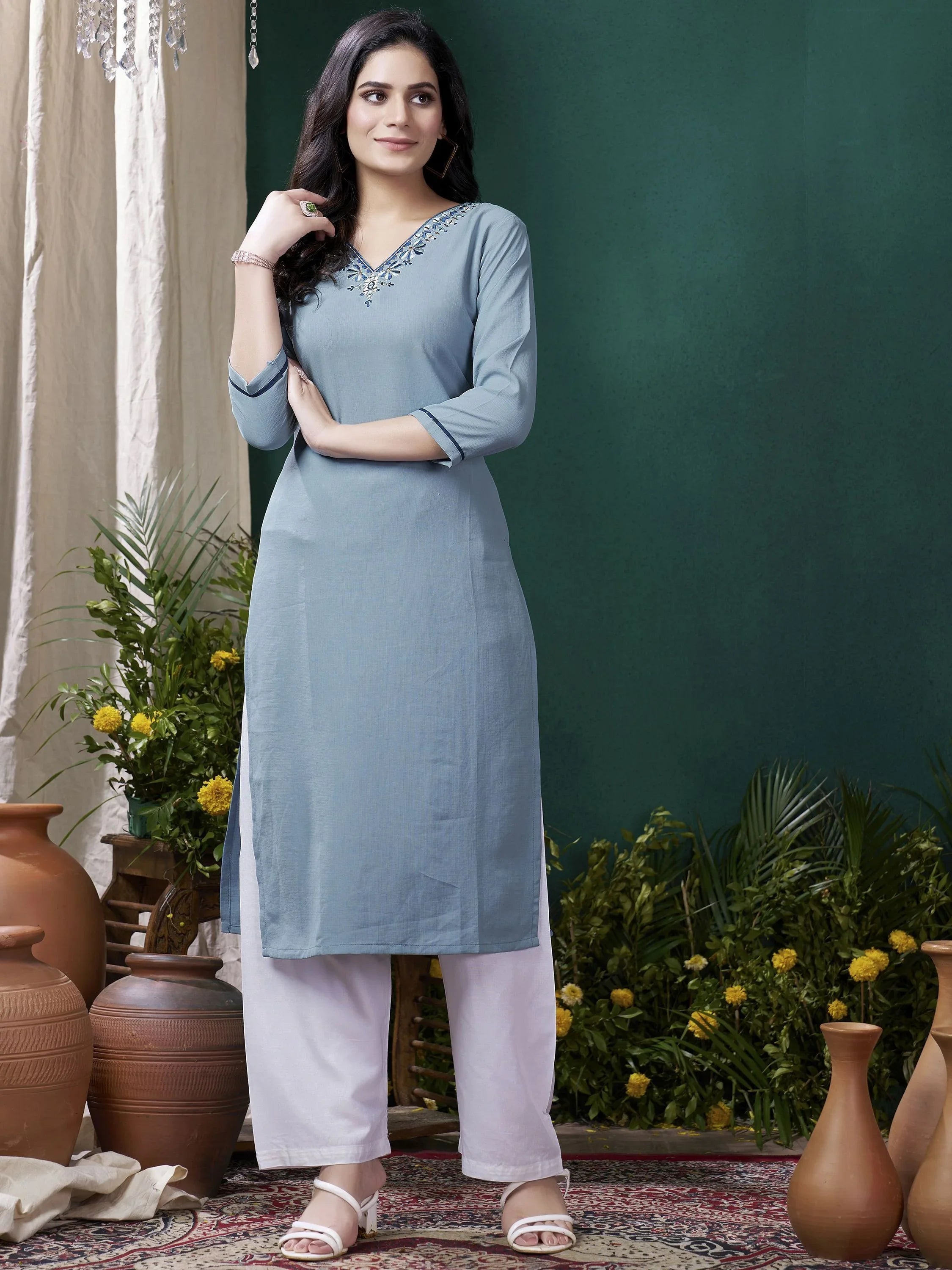 Woman wearing light blue cotton palazzo suit with embroidery, standing indoors with vases