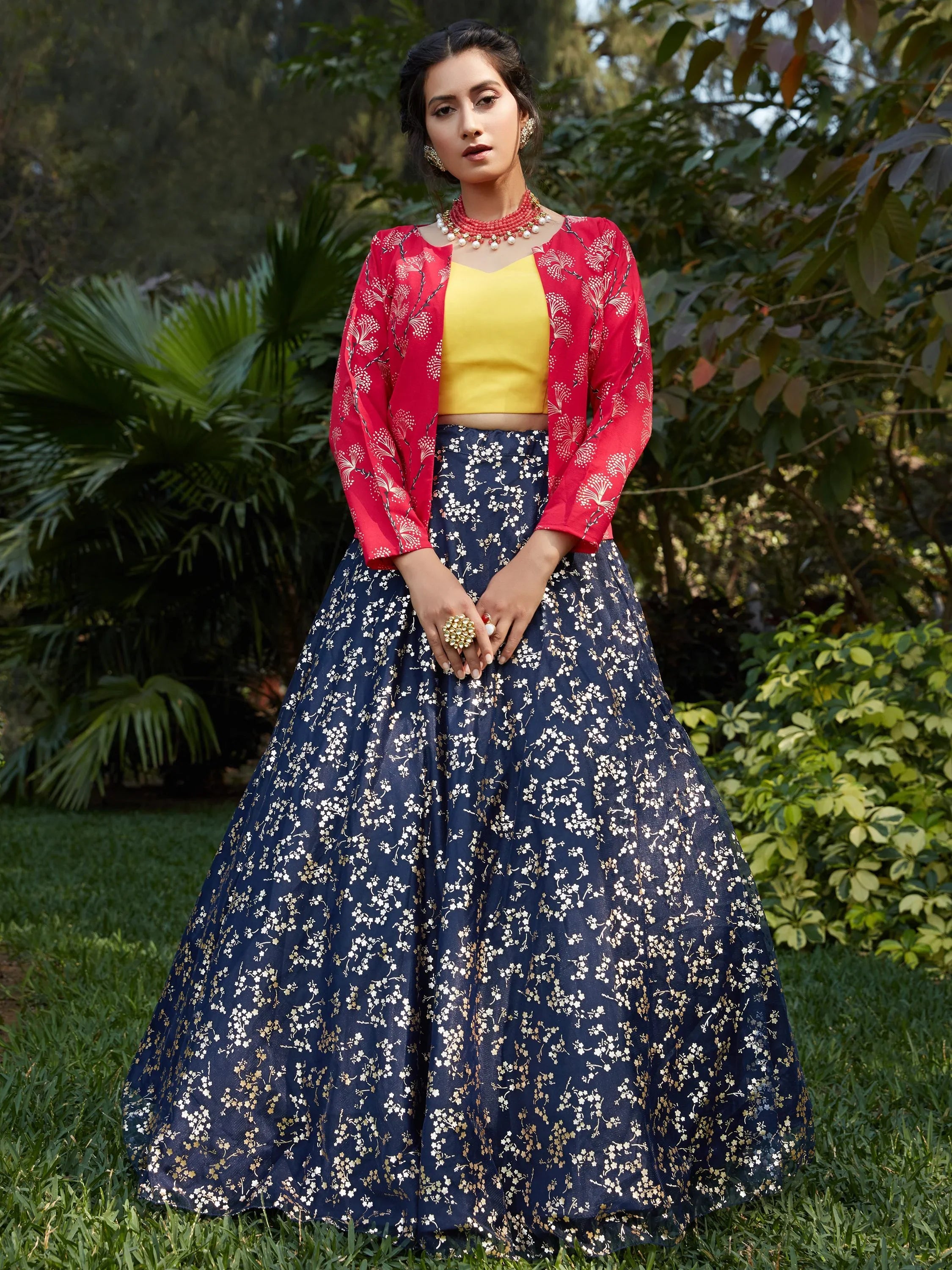 Woman in navy blue floral lehenga with yellow blouse and red jacket, outdoor setting