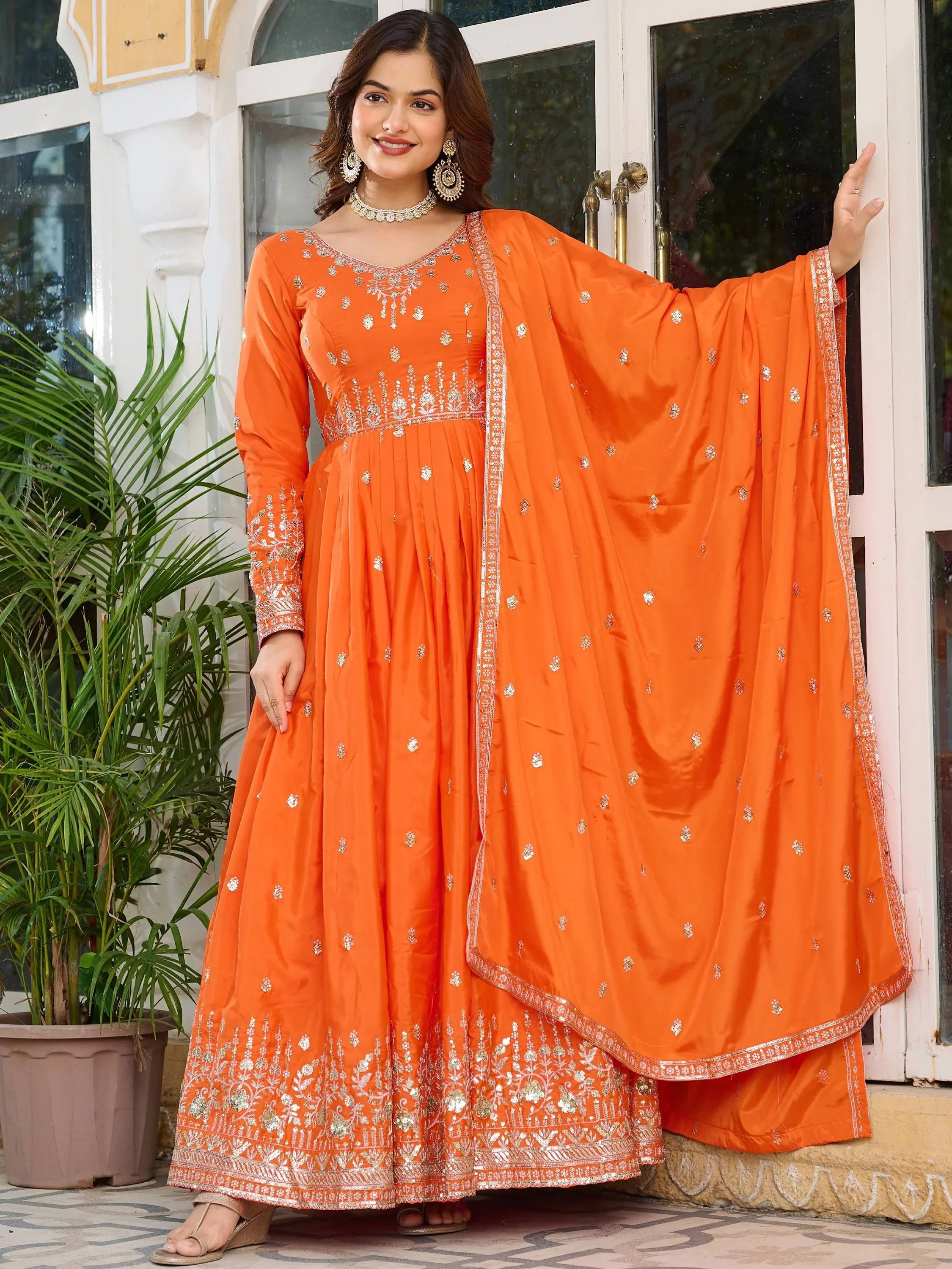 Woman wearing orange embroidered ethnic gown with dupatta, standing outdoors