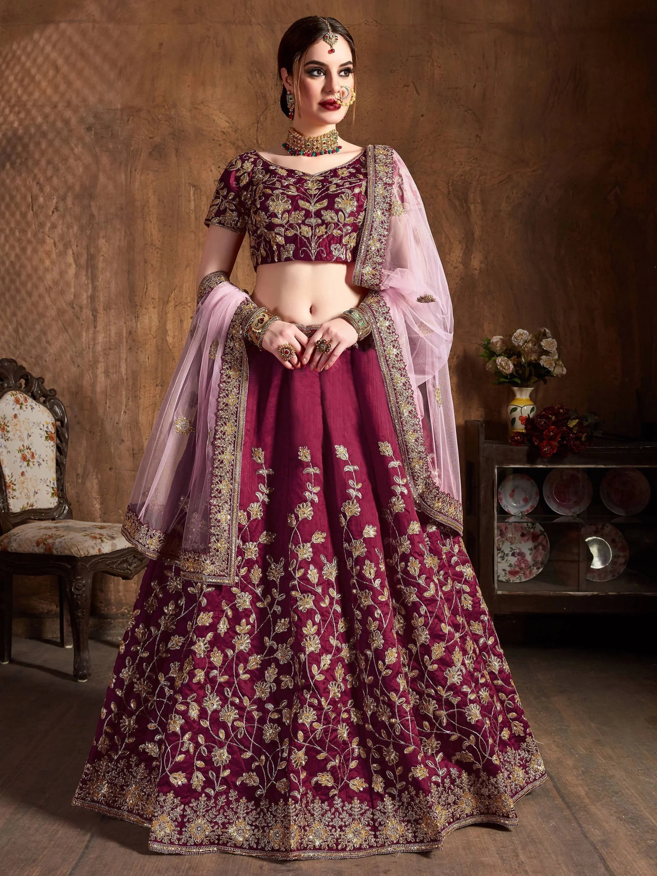 Woman in maroon bridal lehenga choli with gold embroidery and net dupatta, traditional jewelry