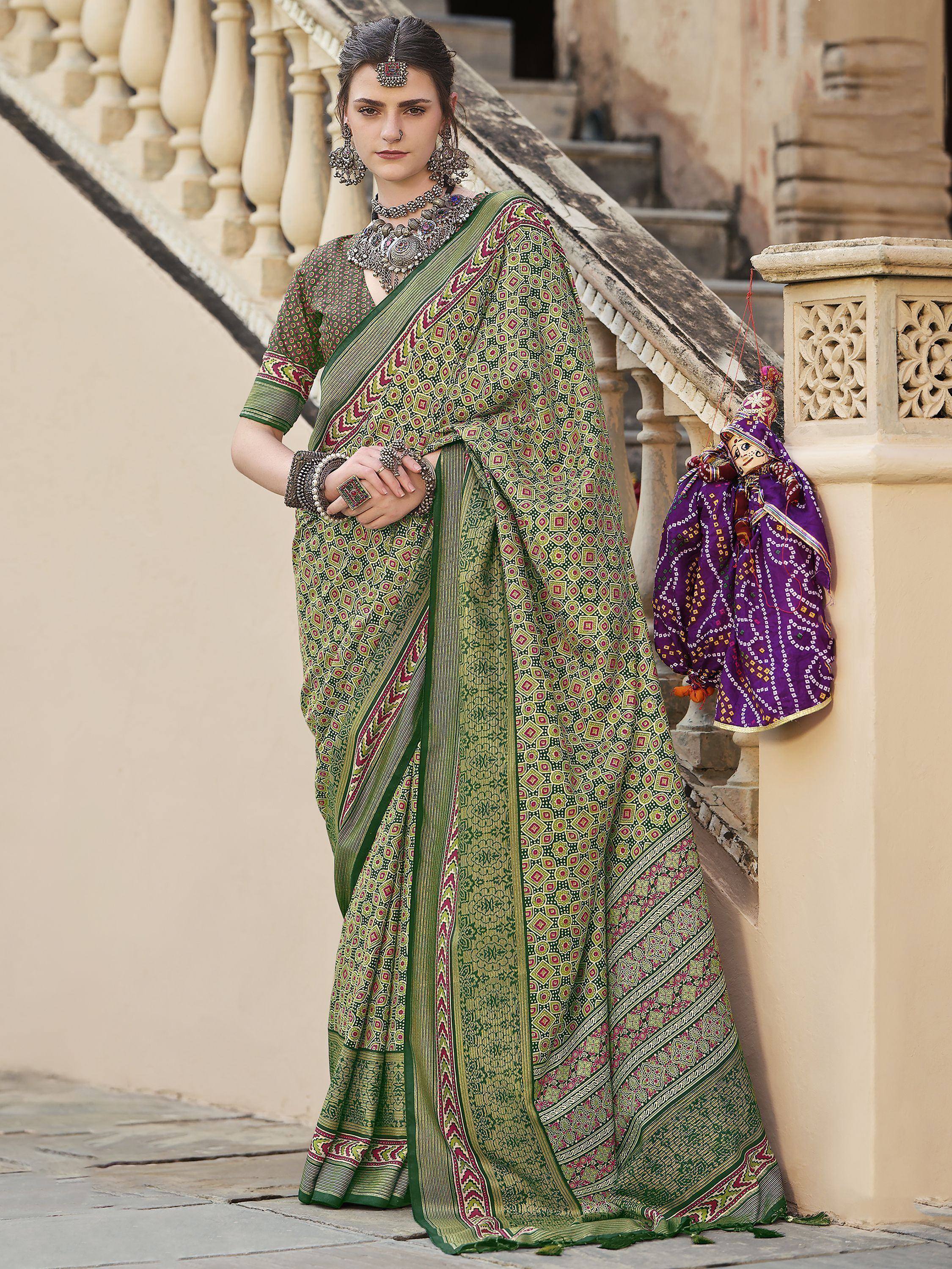 Woman in green printed saree with traditional jewelry, standing by stone stairs, ethnic Indian wear