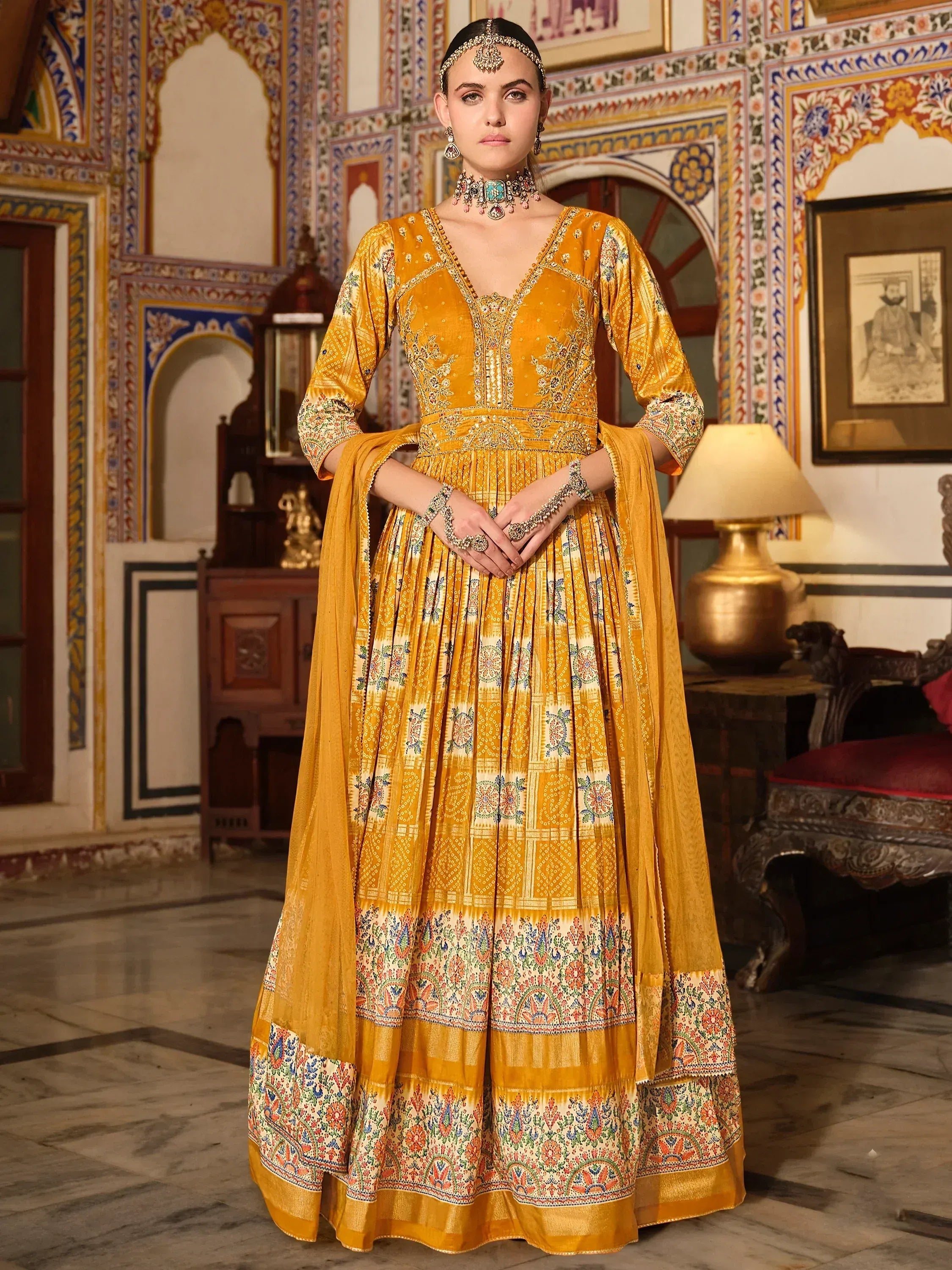 Woman wearing mustard yellow embroidered ethnic gown with floral patterns in royal interior setting