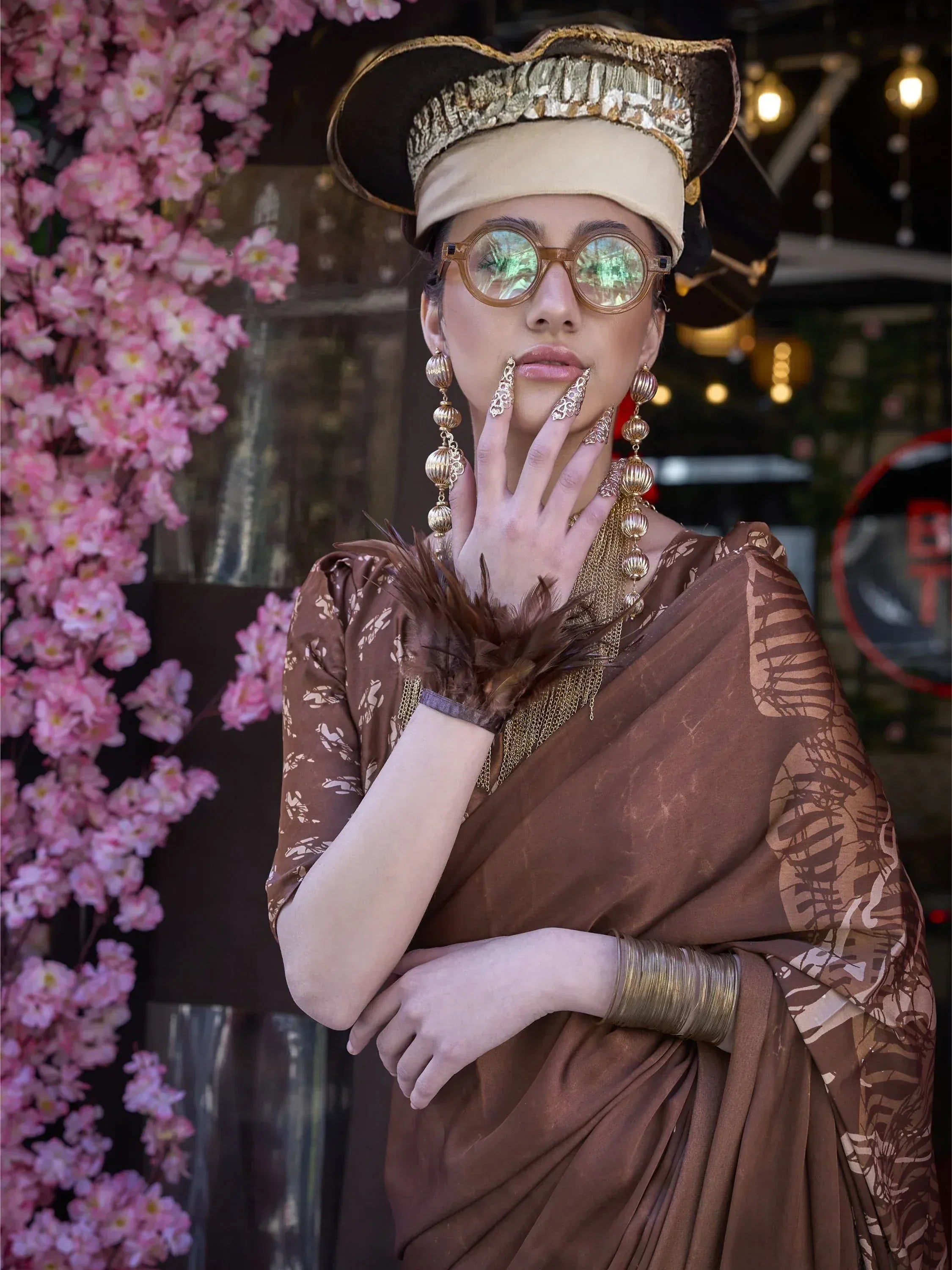 Woman in brown printed saree with gold jewelry and ornate hat, styled for ethnic fashion