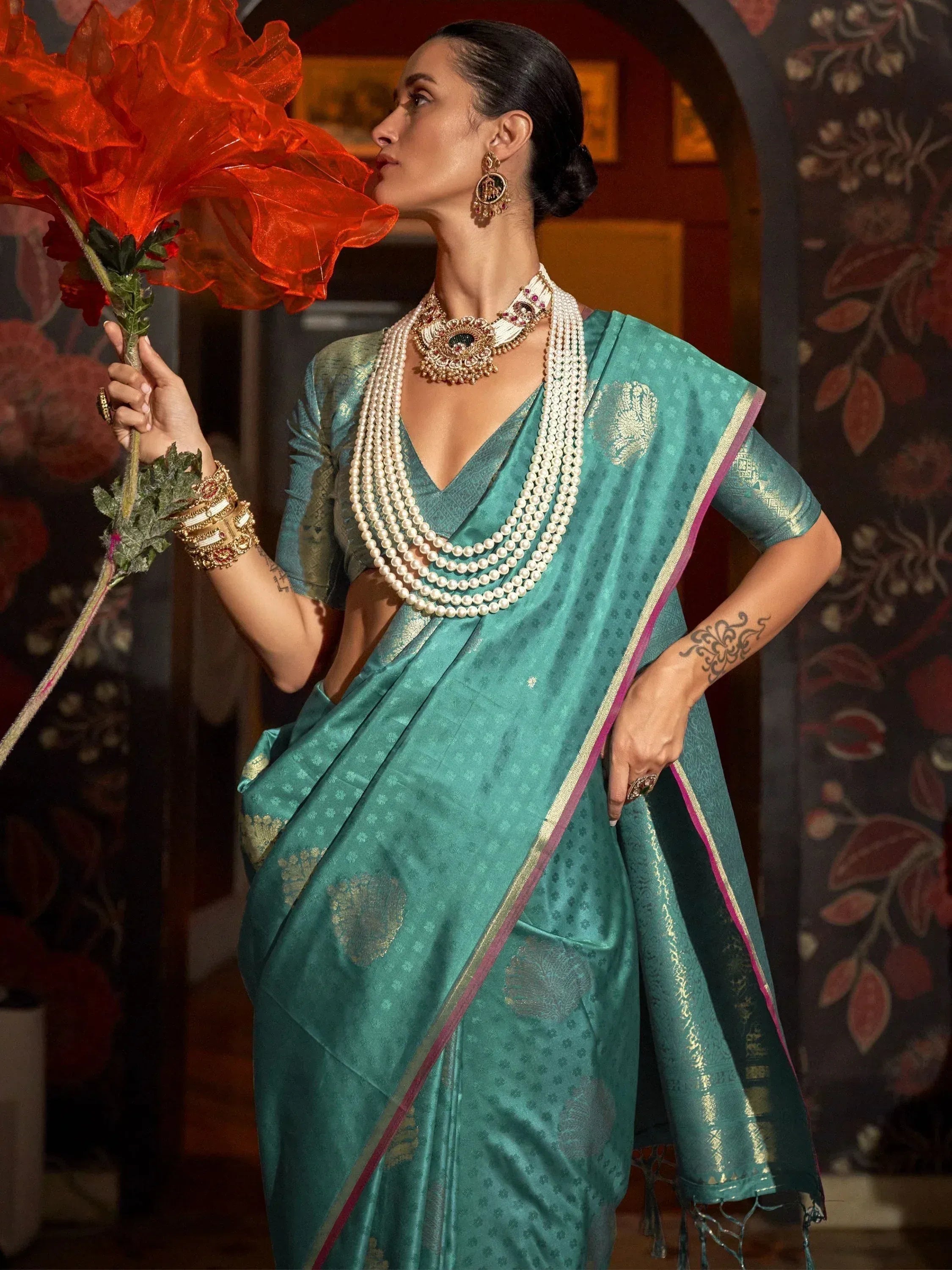 Teal designer saree with gold motifs, pearl necklace, and statement earrings for Indian ethnic wear