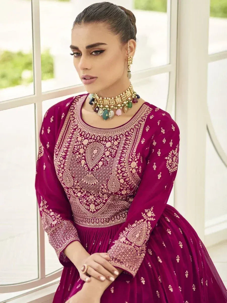 Woman in magenta embroidered ethnic gown with traditional jewelry near window