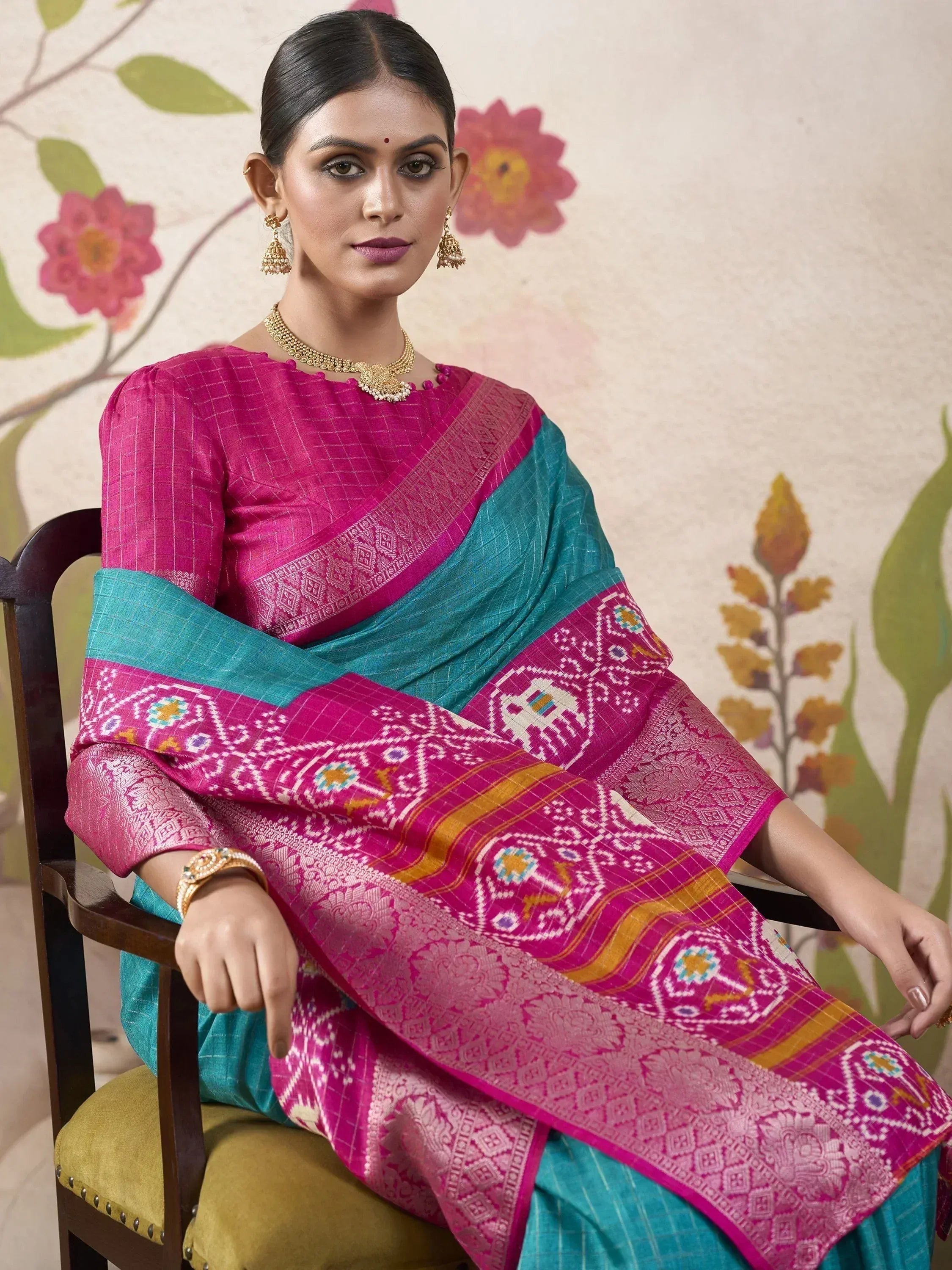 Woman in vibrant pink and teal designer saree with intricate ikat patterns, perfect for ethnic occasions