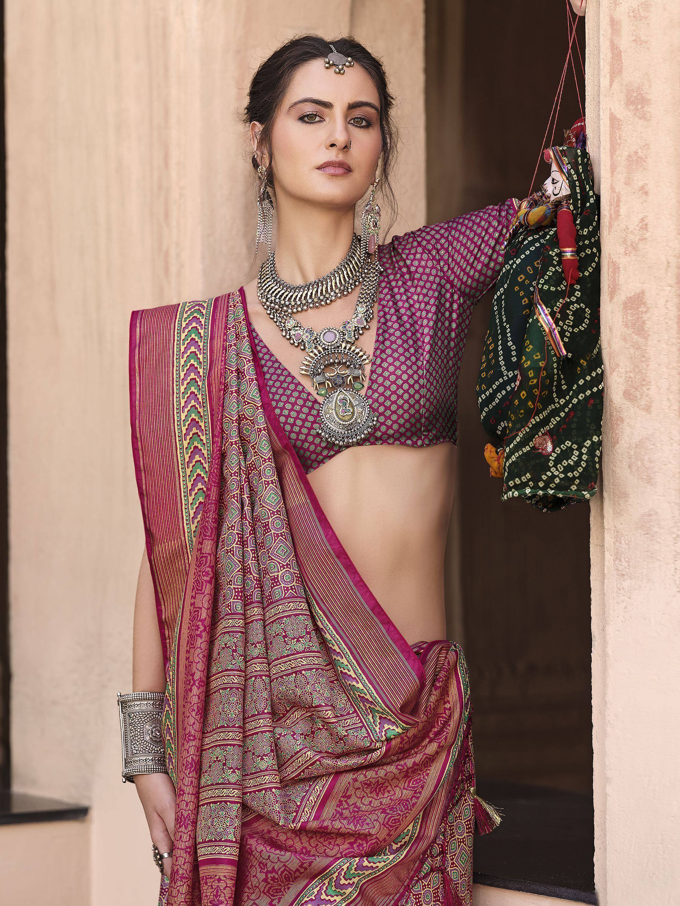 Woman in maroon ethnic saree with intricate patterns, traditional jewelry, and decorative puppet, showcasing Indian designer wear.
