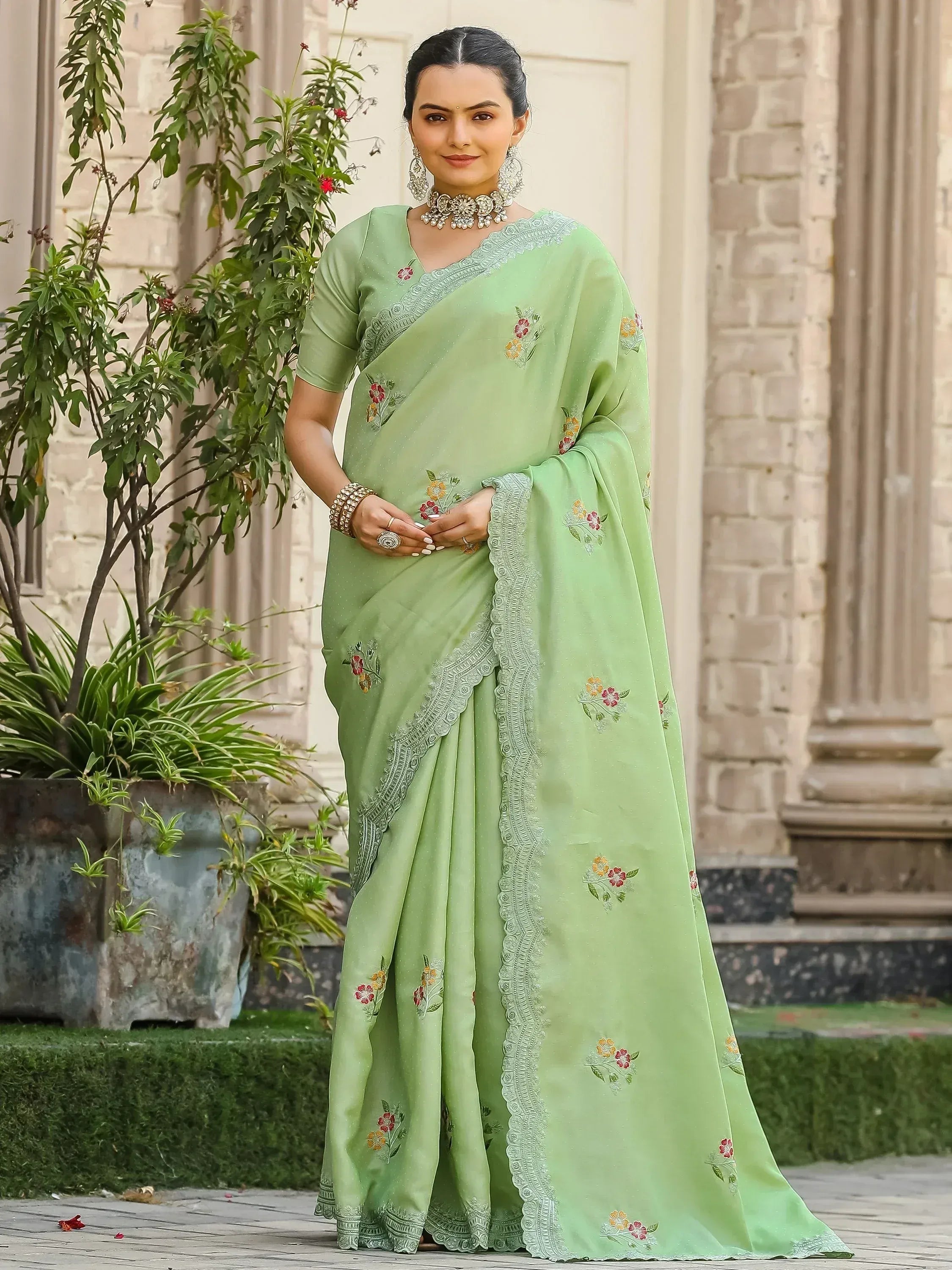 Light green embroidered saree with floral motifs and lace border, styled with traditional jewelry for ethnic wear