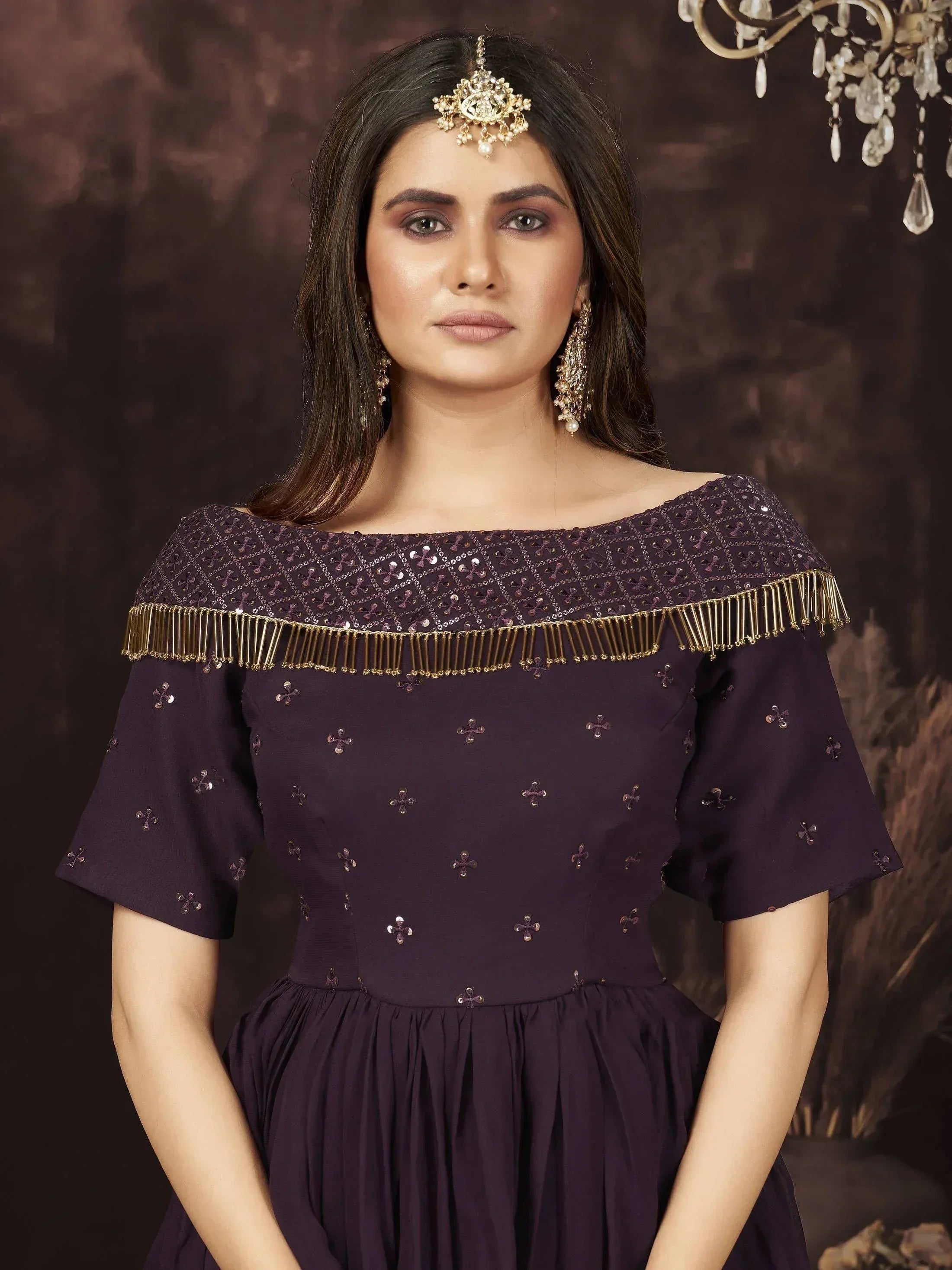 Purple ethnic gown with gold fringe and sequin embroidery, paired with traditional jewelry for festive occasions.