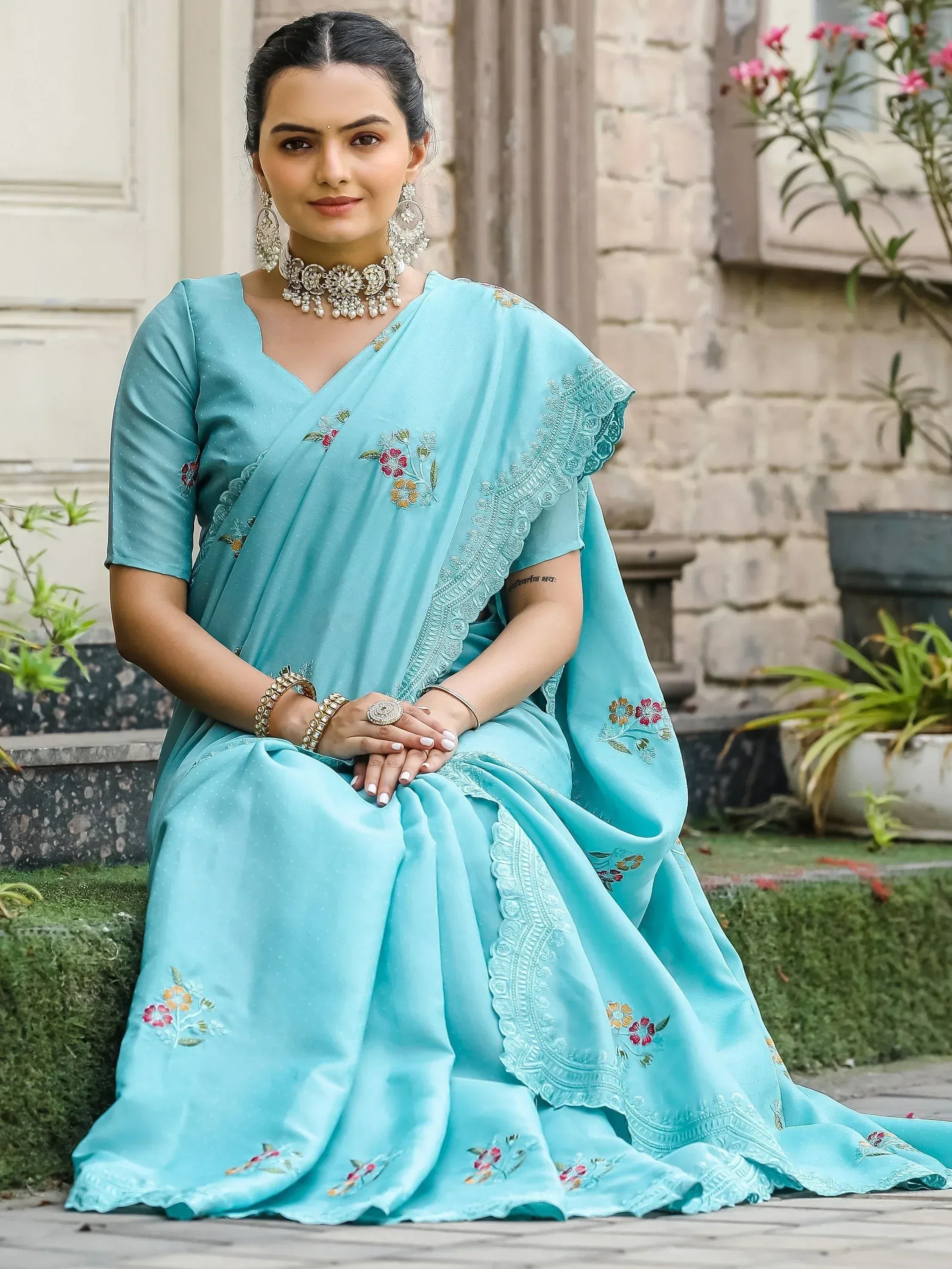 Woman in elegant turquoise saree with floral embroidery and scalloped border, styled with traditional jewelry