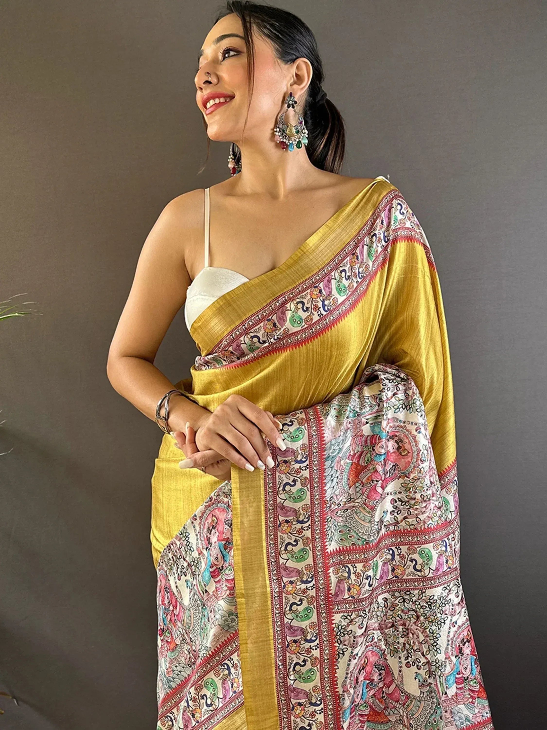 Woman in vibrant yellow saree with colorful paisley print, styled with white blouse and statement earrings