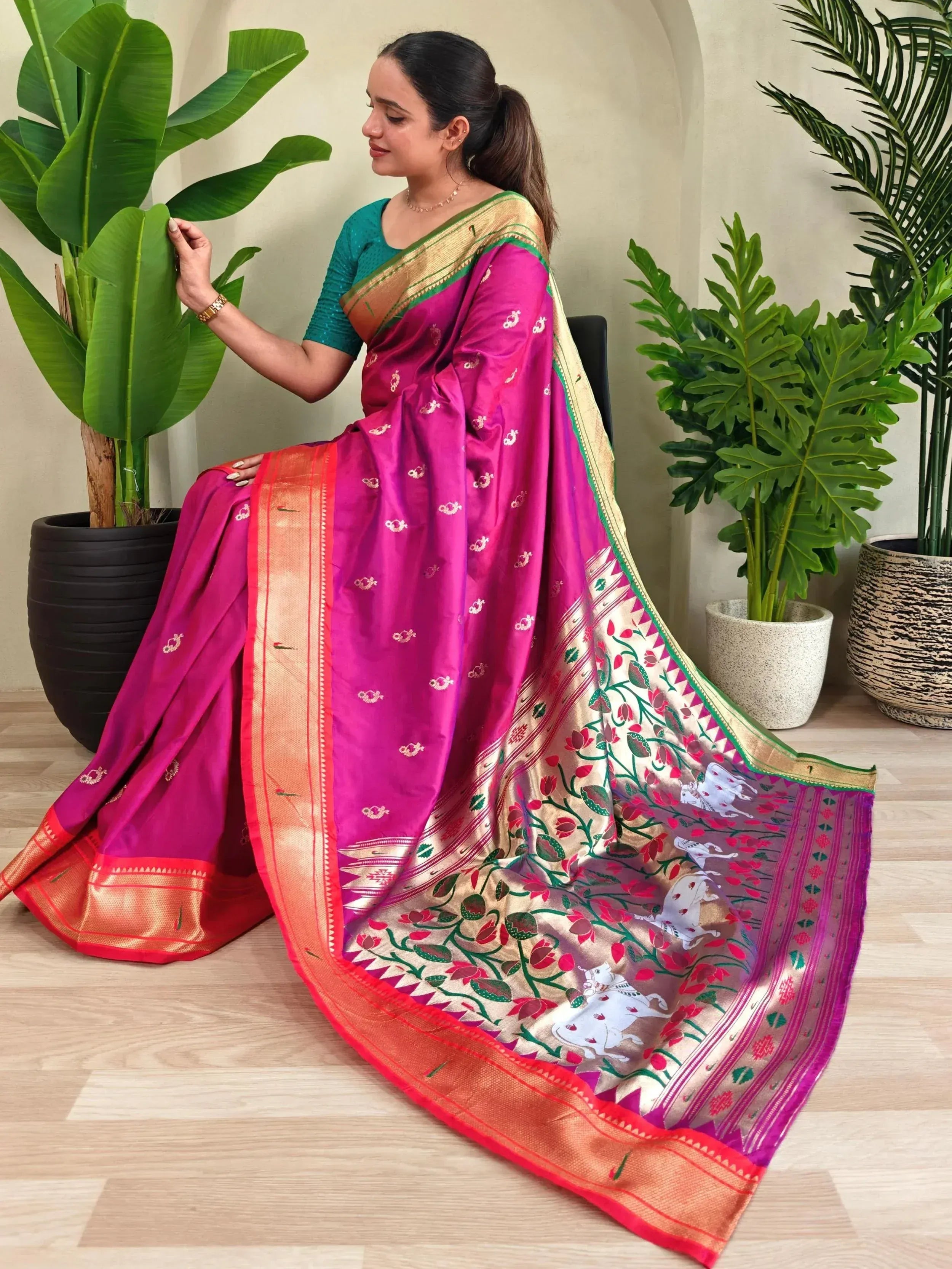 Vibrant pink designer saree with floral and bull motifs, gold border, paired with teal blouse, ideal for Indian ethnic occasions.