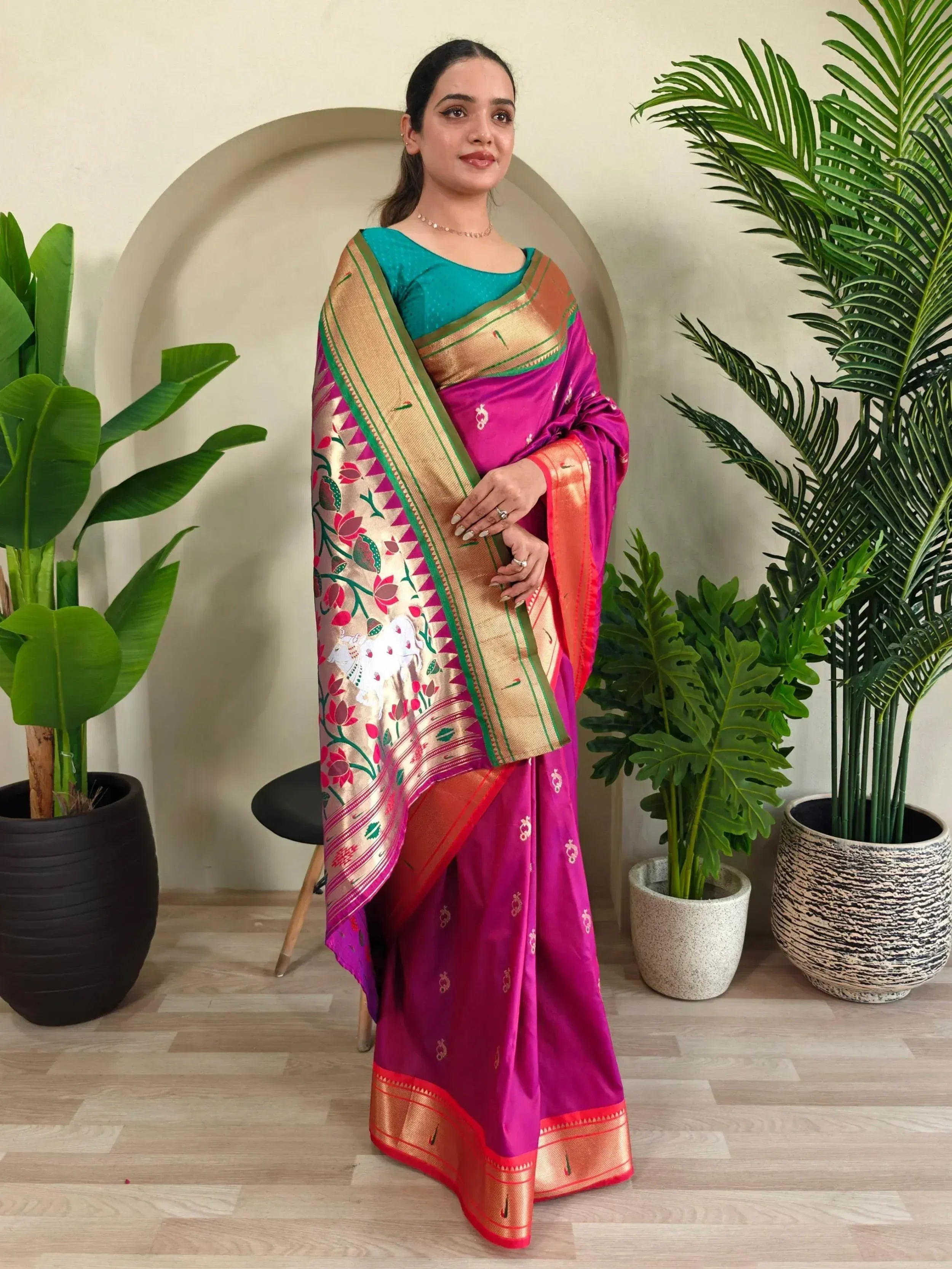 Woman in vibrant pink silk saree with gold border and floral motifs, paired with teal blouse, ideal for Indian ethnic occasions.