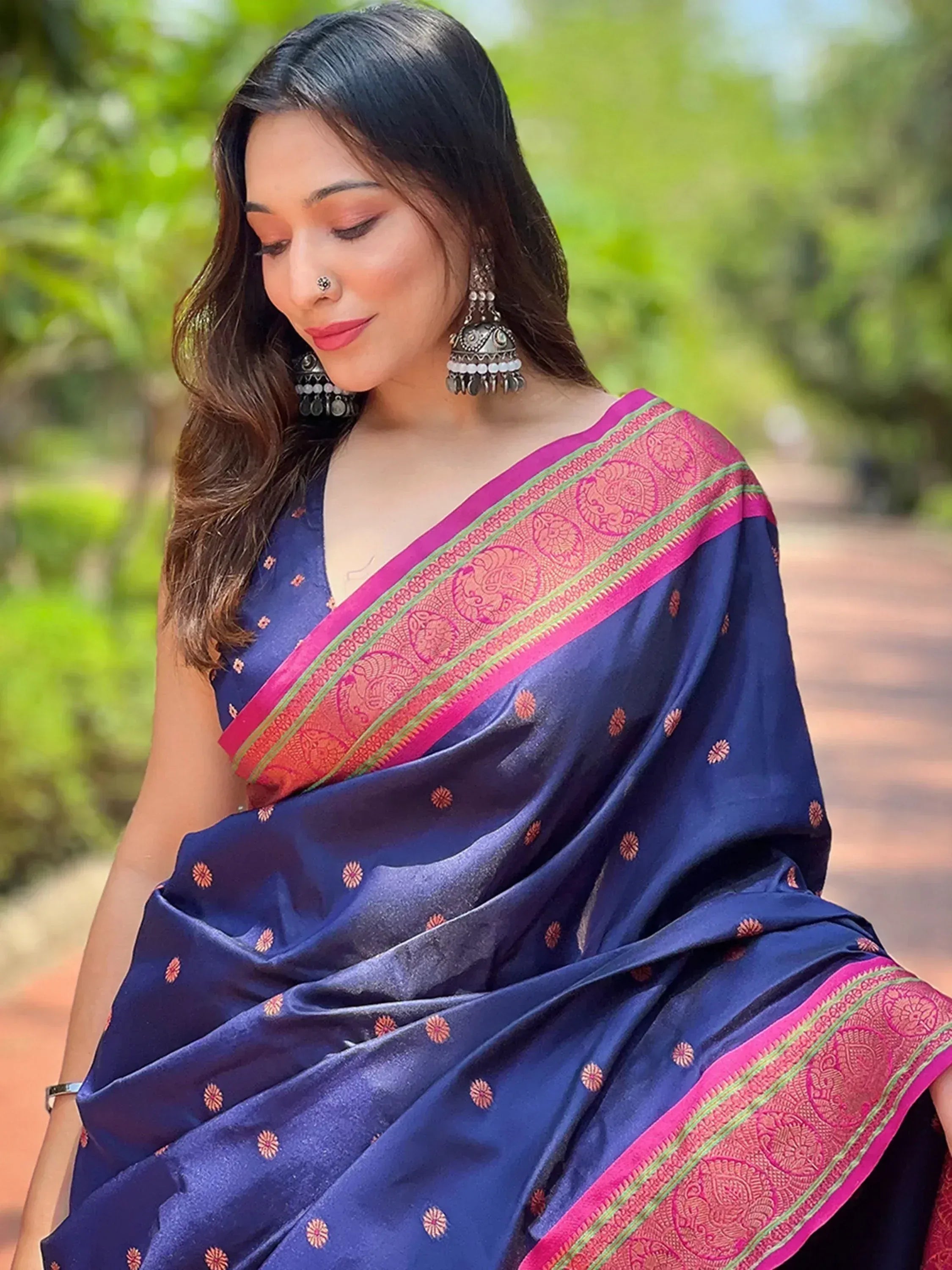 Woman in navy blue saree with pink border and gold motifs, styled with jhumka earrings for ethnic wear
