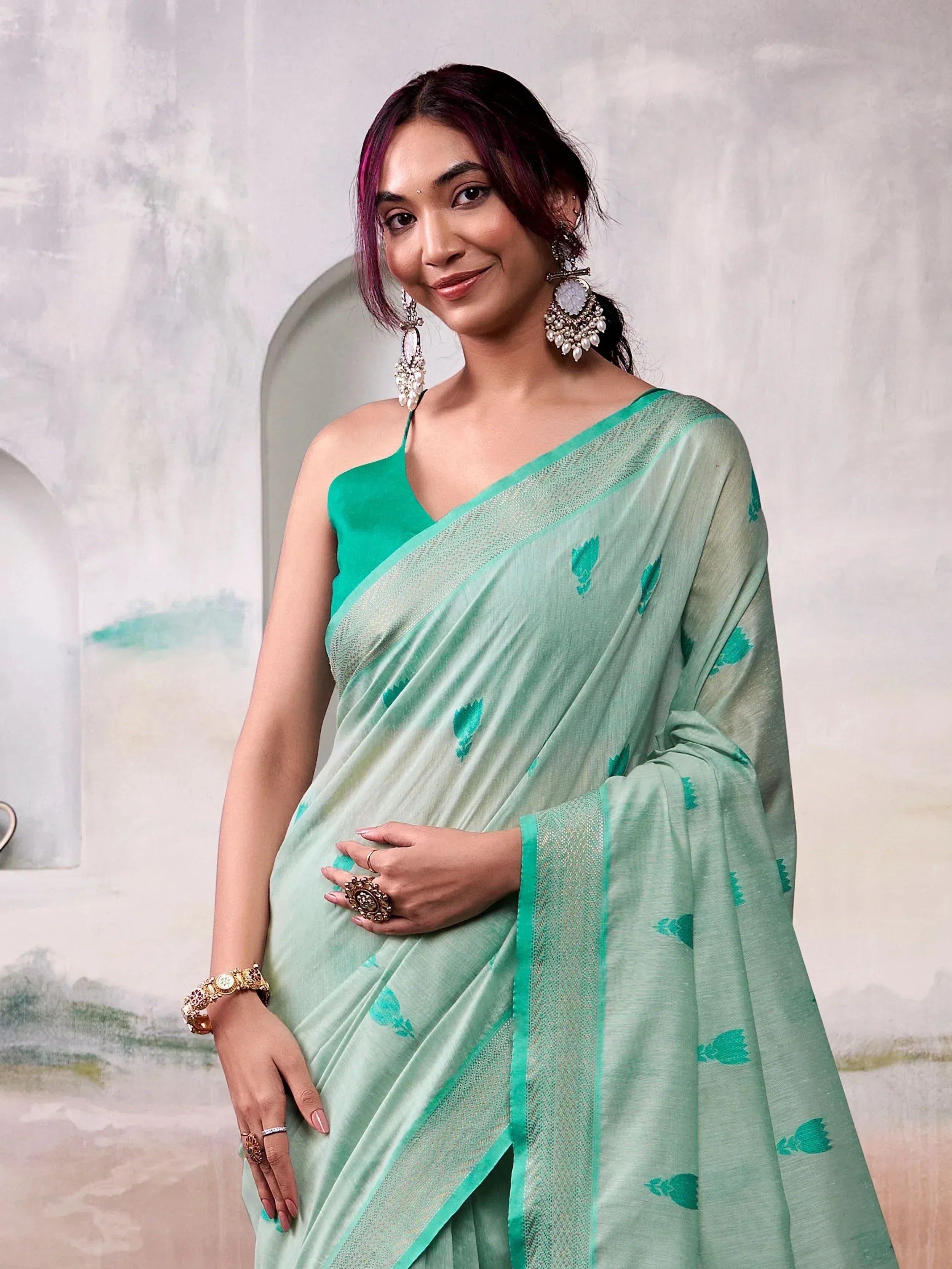 Woman in mint green saree with leaf print, paired with emerald blouse and statement jewelry