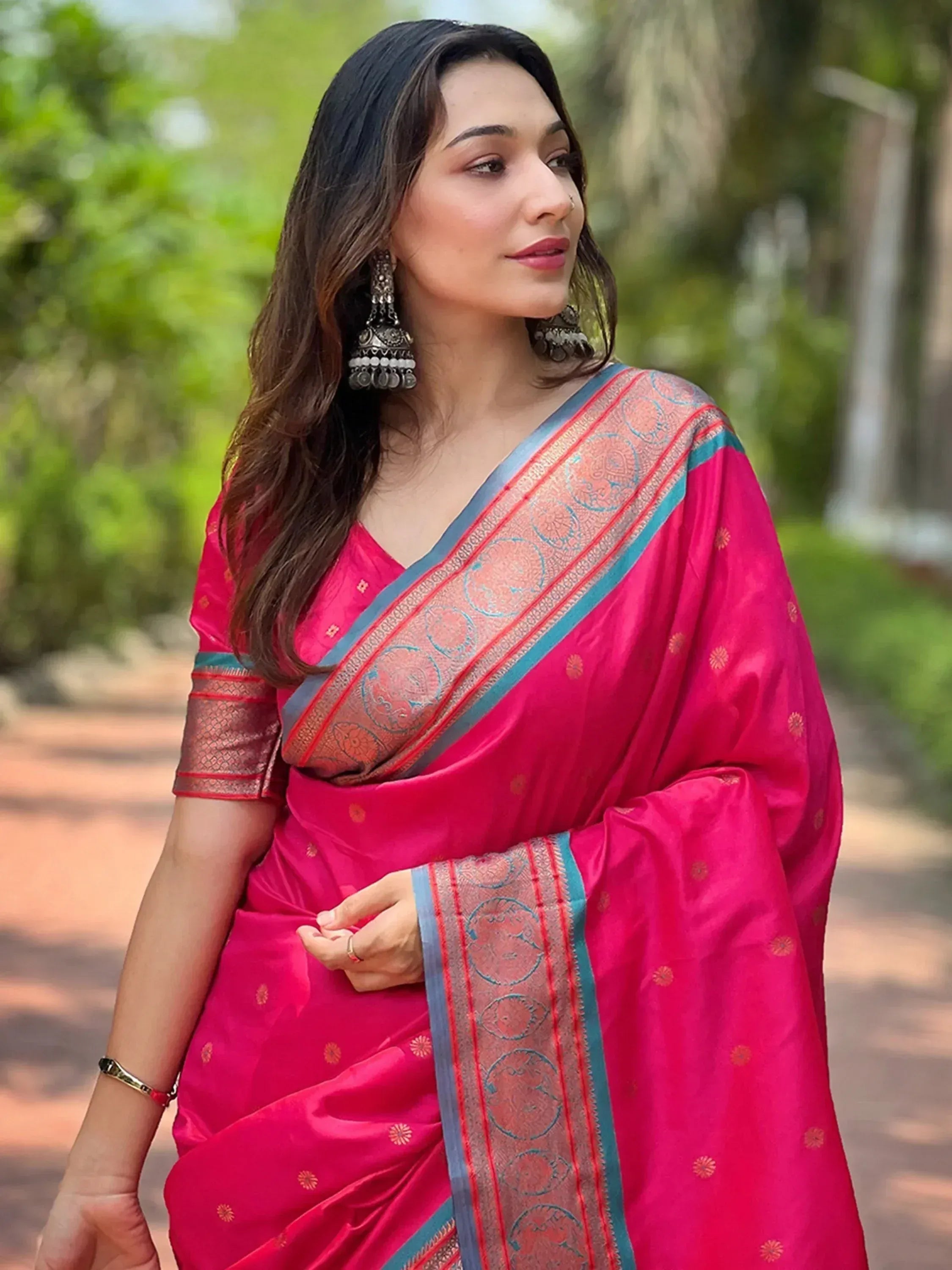 Woman in vibrant pink designer saree with blue border and gold motifs, styled with jhumka earrings for ethnic wear
