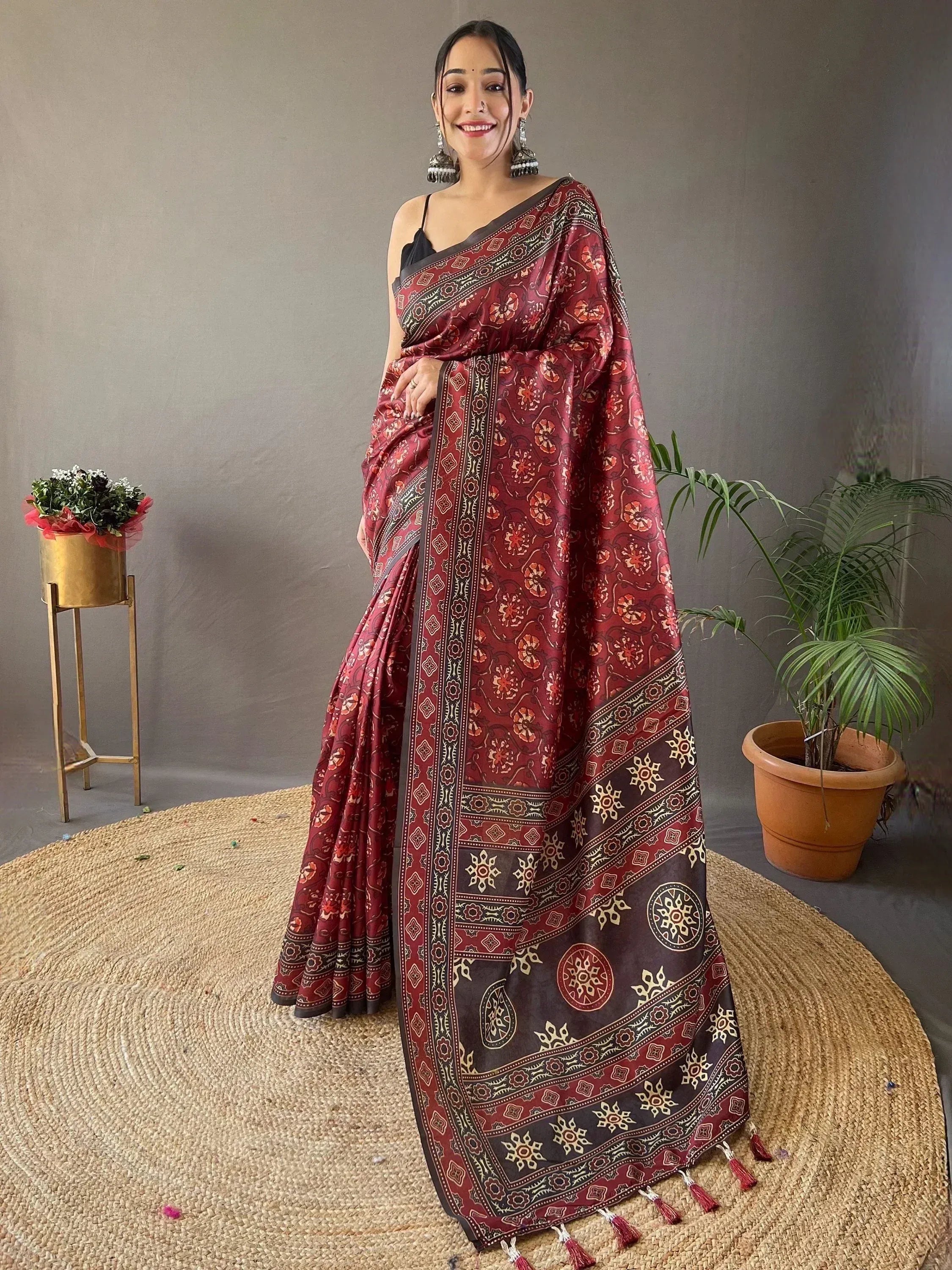Woman in maroon floral print saree with gold border and tassels, styled with black blouse and jhumka earrings