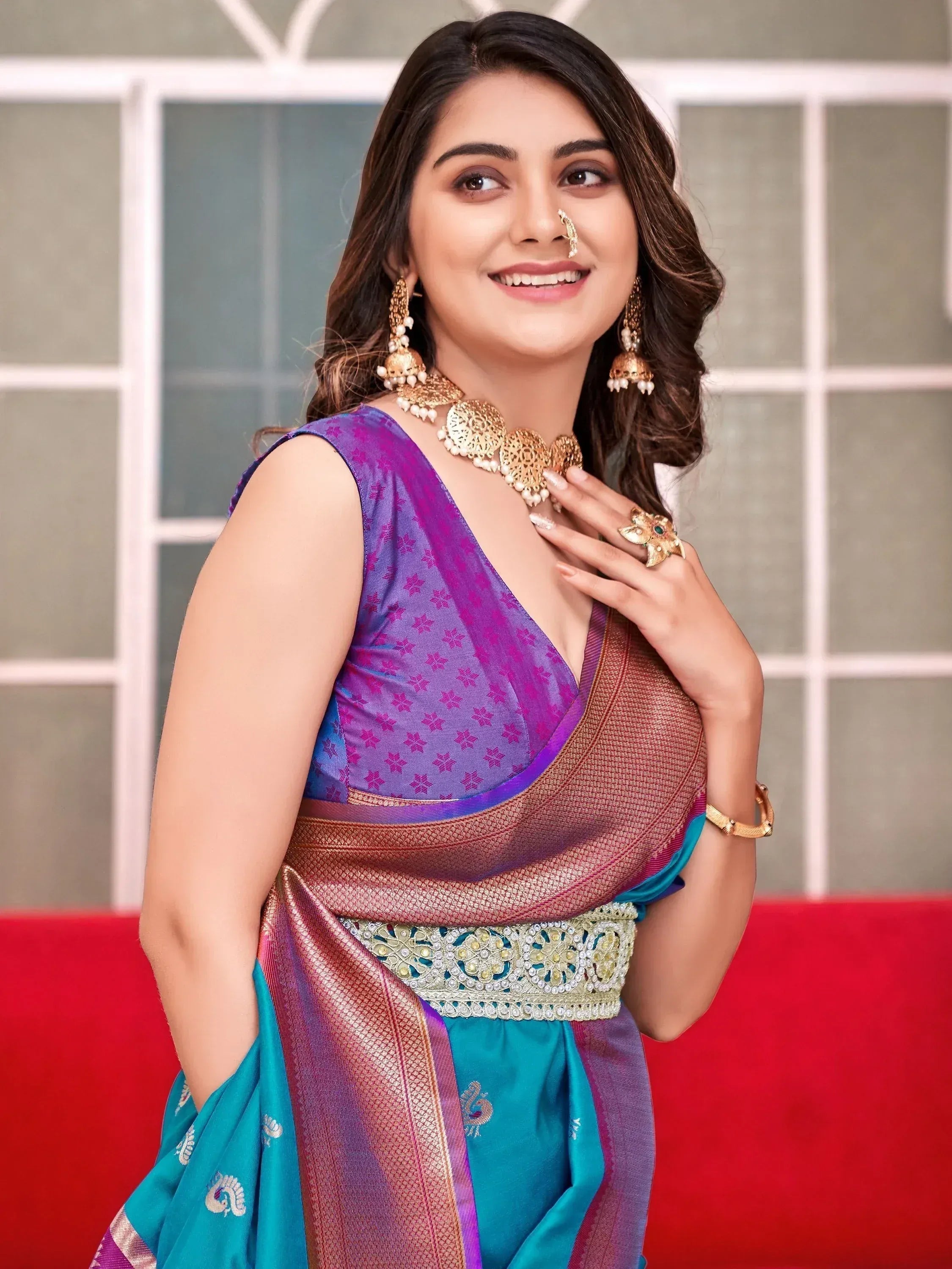 Woman in vibrant purple and teal designer saree with gold jewelry, perfect for Indian ethnic wear occasions.