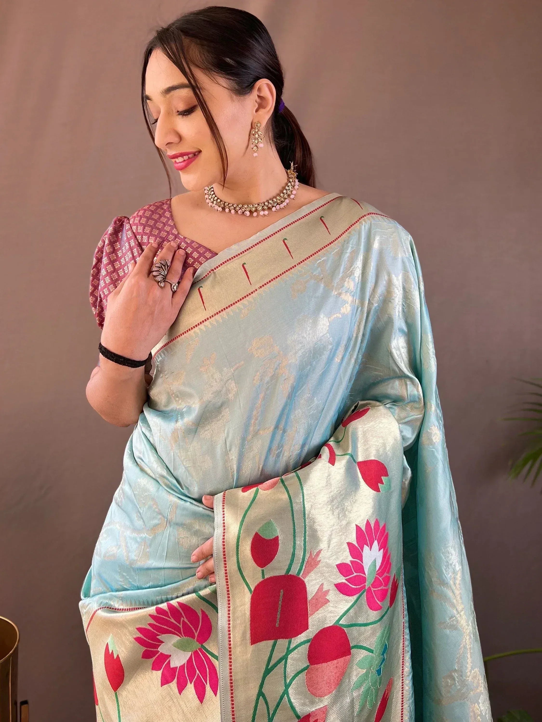 Woman in light blue saree with pink floral border, paired with patterned blouse and traditional jewelry