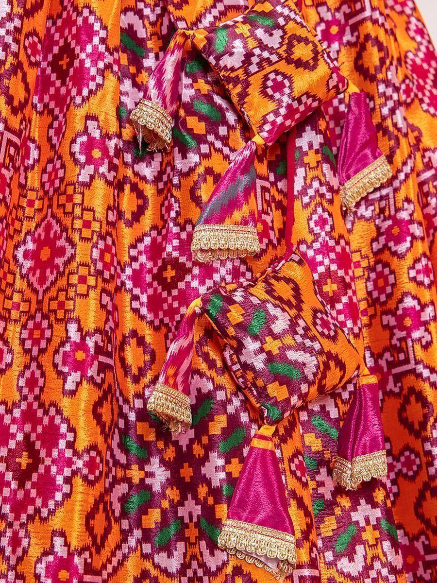 Vibrant ethnic lehenga with geometric ikat print, gold trim, and tassels in pink, orange, green