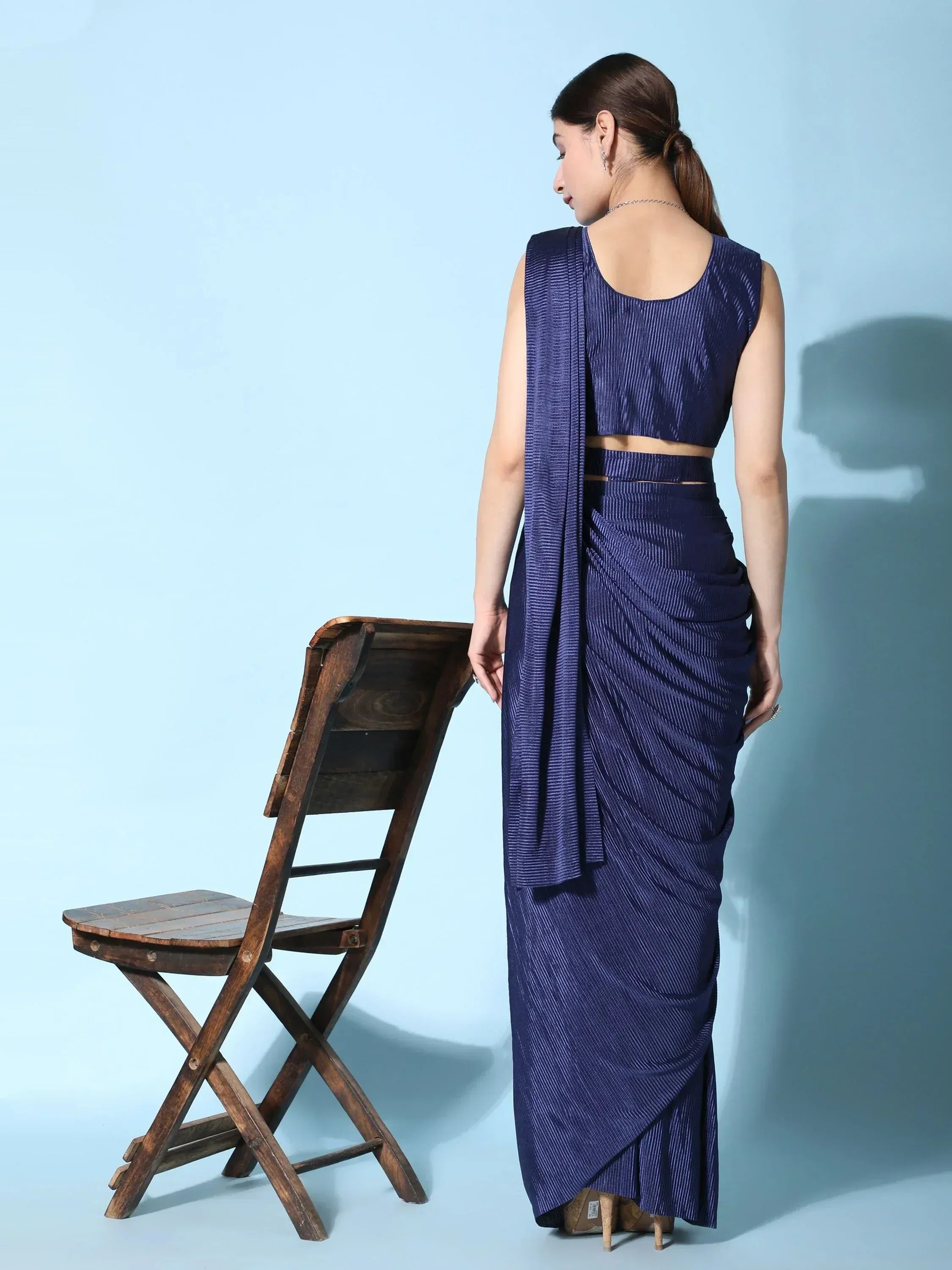 Navy blue pleated saree with sleeveless blouse, ethnic wear for women, stylish drape against blue backdrop