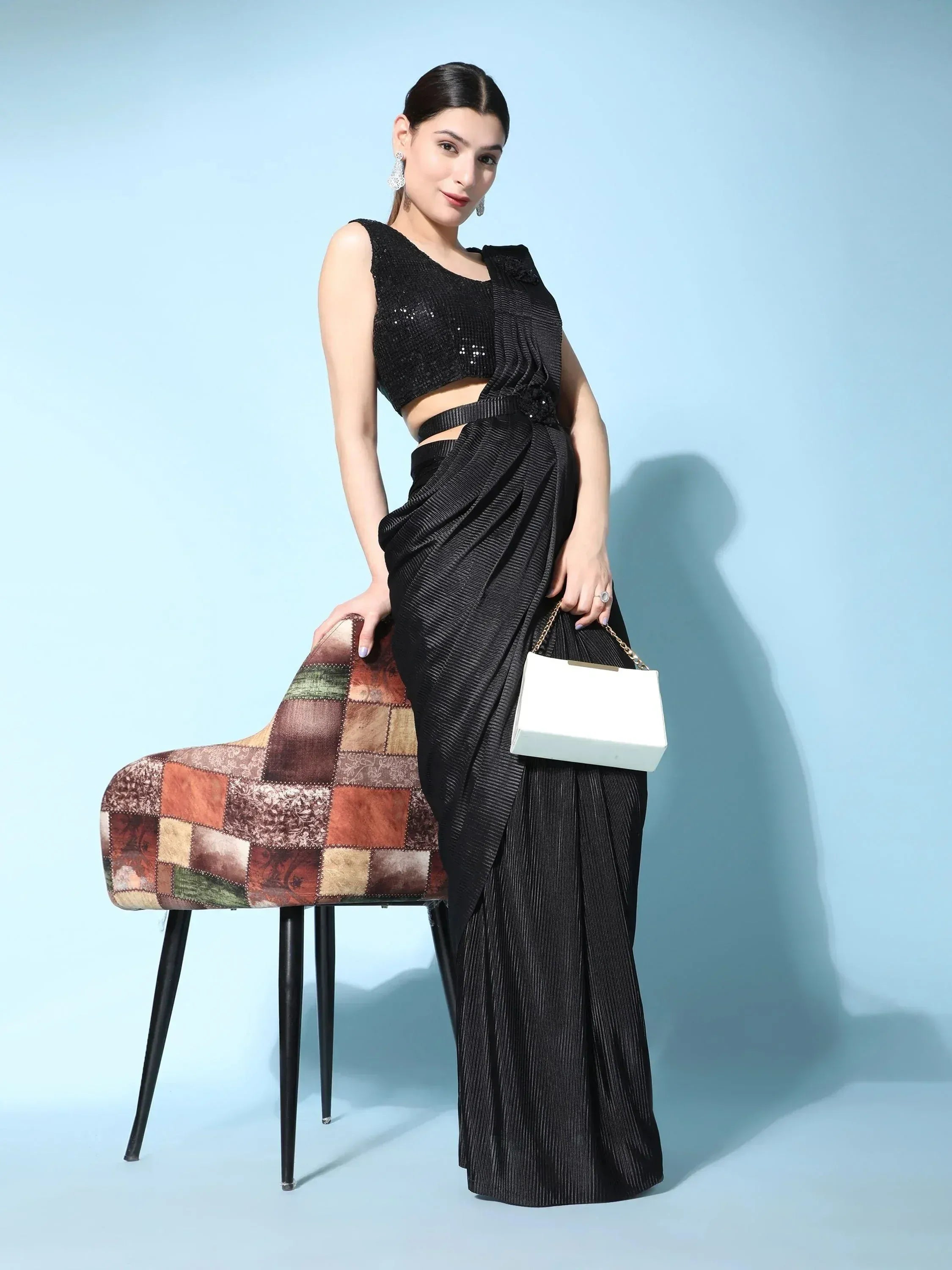 Woman in black sequin crop top and pleated drape saree with white clutch, stylish ethnic wear