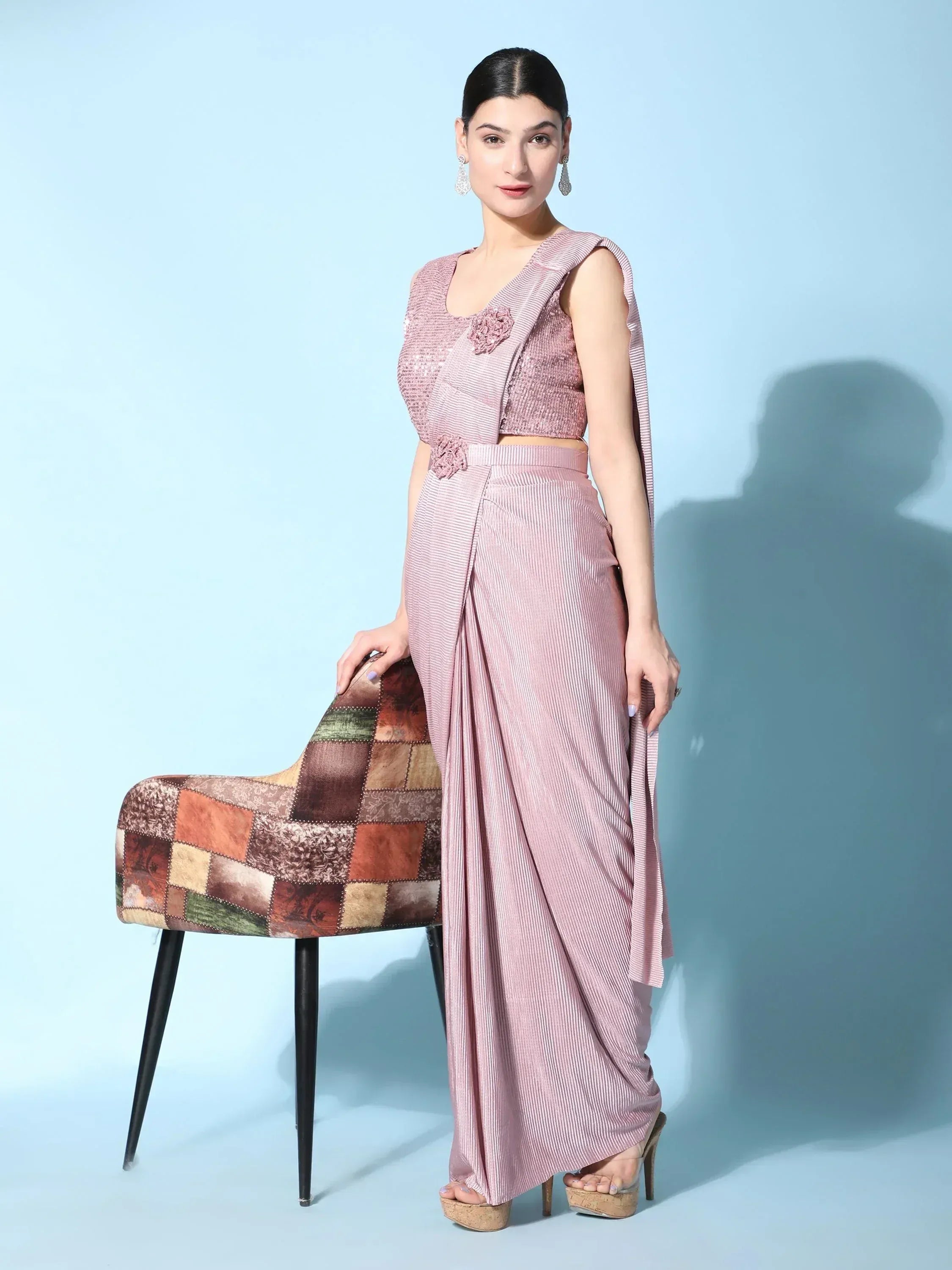 Pink striped ethnic gown with floral embellishments, styled with high heels and a patchwork chair