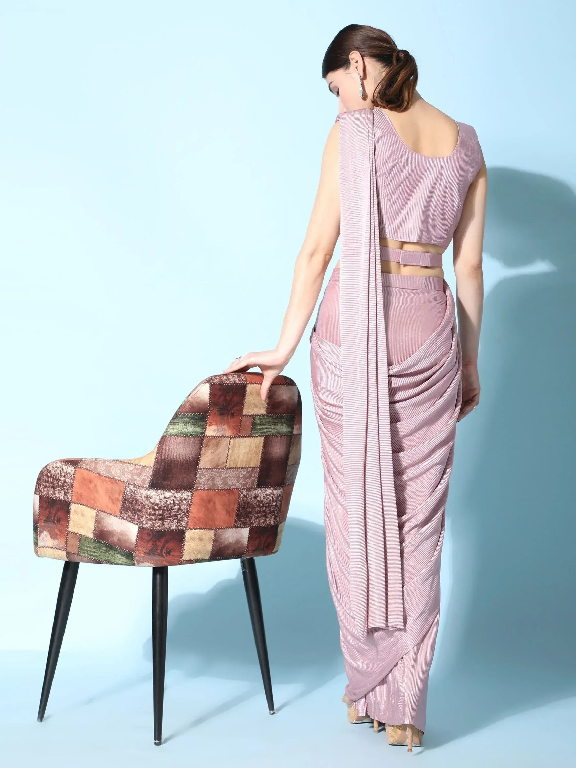 Elegant pink striped saree with modern drape, paired with a stylish patchwork chair