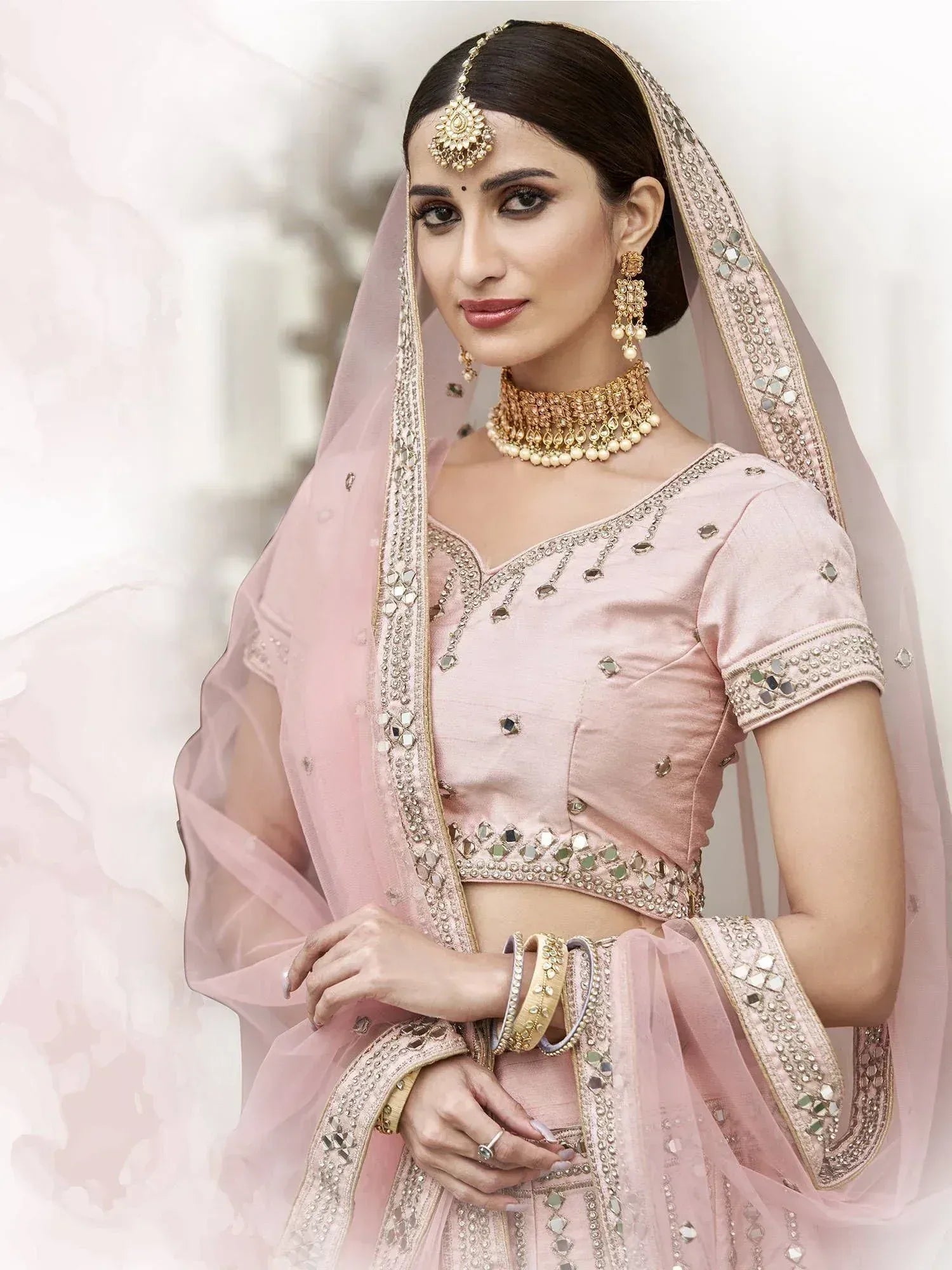 Pink designer lehenga choli with mirror work, gold jewelry, and dupatta for Indian weddings