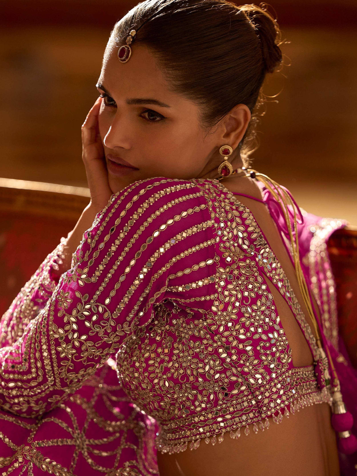 Fuchsia designer lehenga choli with intricate gold mirror work and traditional Indian jewelry