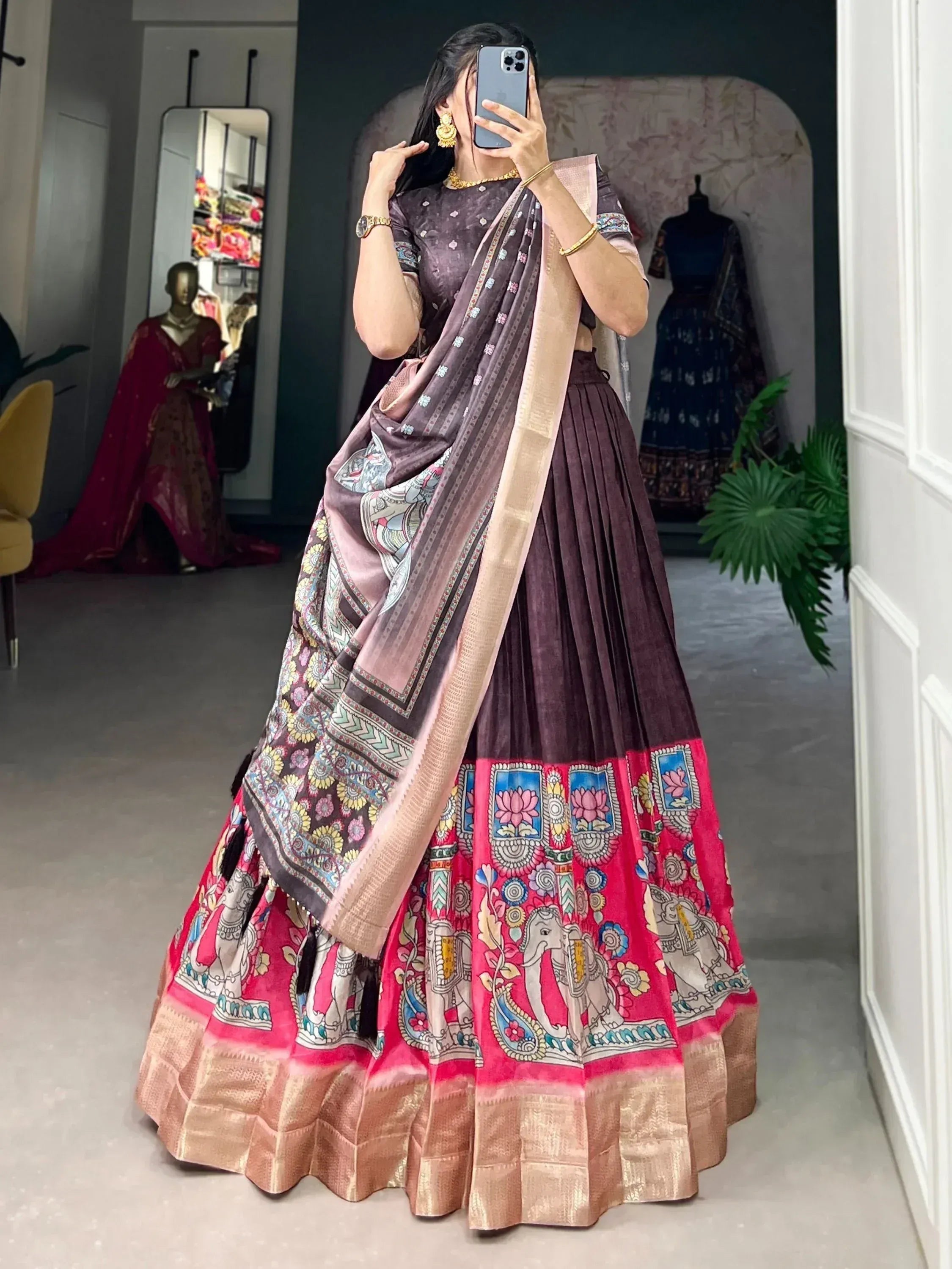 Woman in purple and pink printed lehenga choli with elephant motifs, taking mirror selfie in boutique