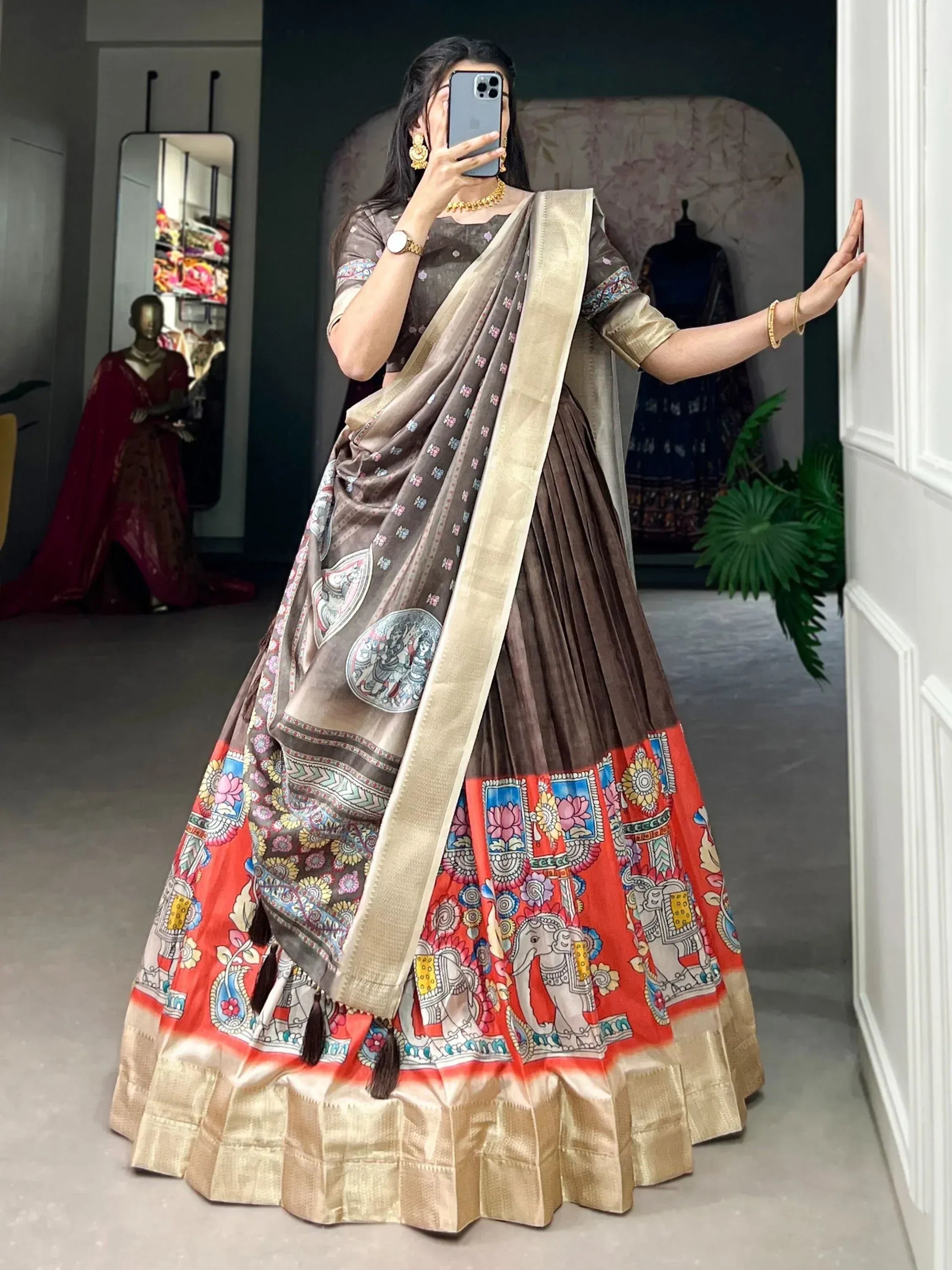 Woman in brown and red printed lehenga choli with elephant motifs, gold border, and matching dupatta, taking mirror selfie.