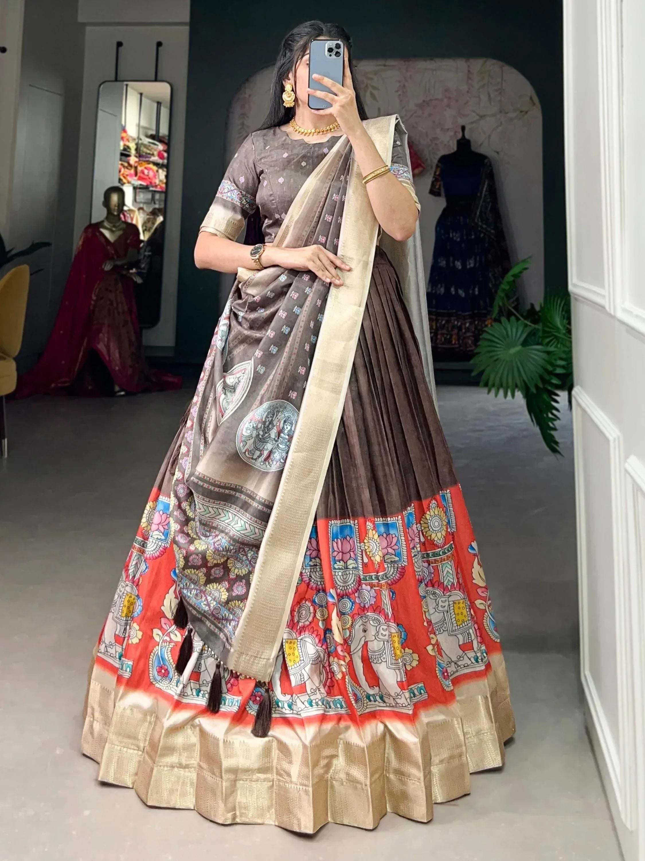 Woman wearing printed ethnic lehenga choli with saree dupatta, gold jewelry, mirror selfie in boutique