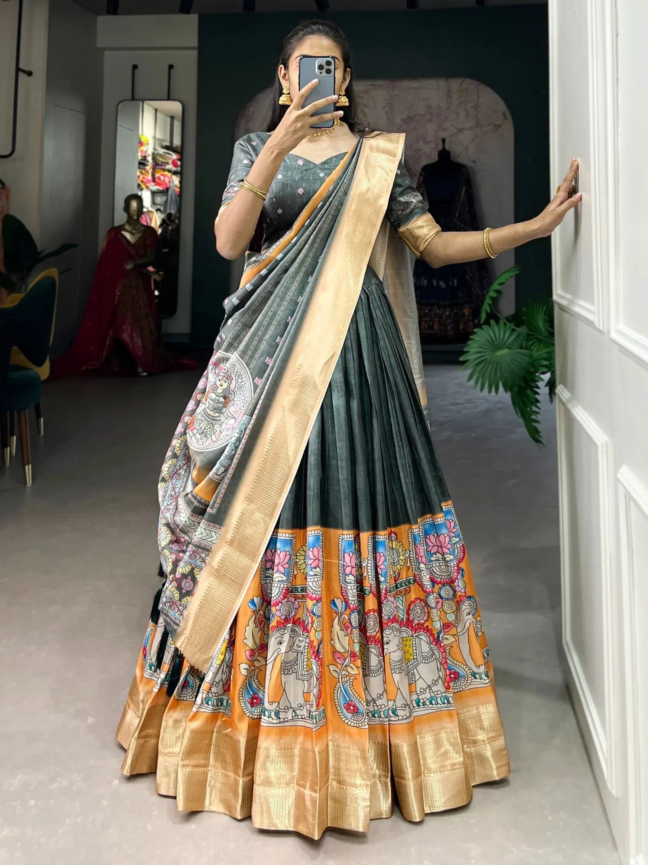 Woman in grey and orange printed lehenga choli with elephant motifs, gold border, mirror selfie in boutique