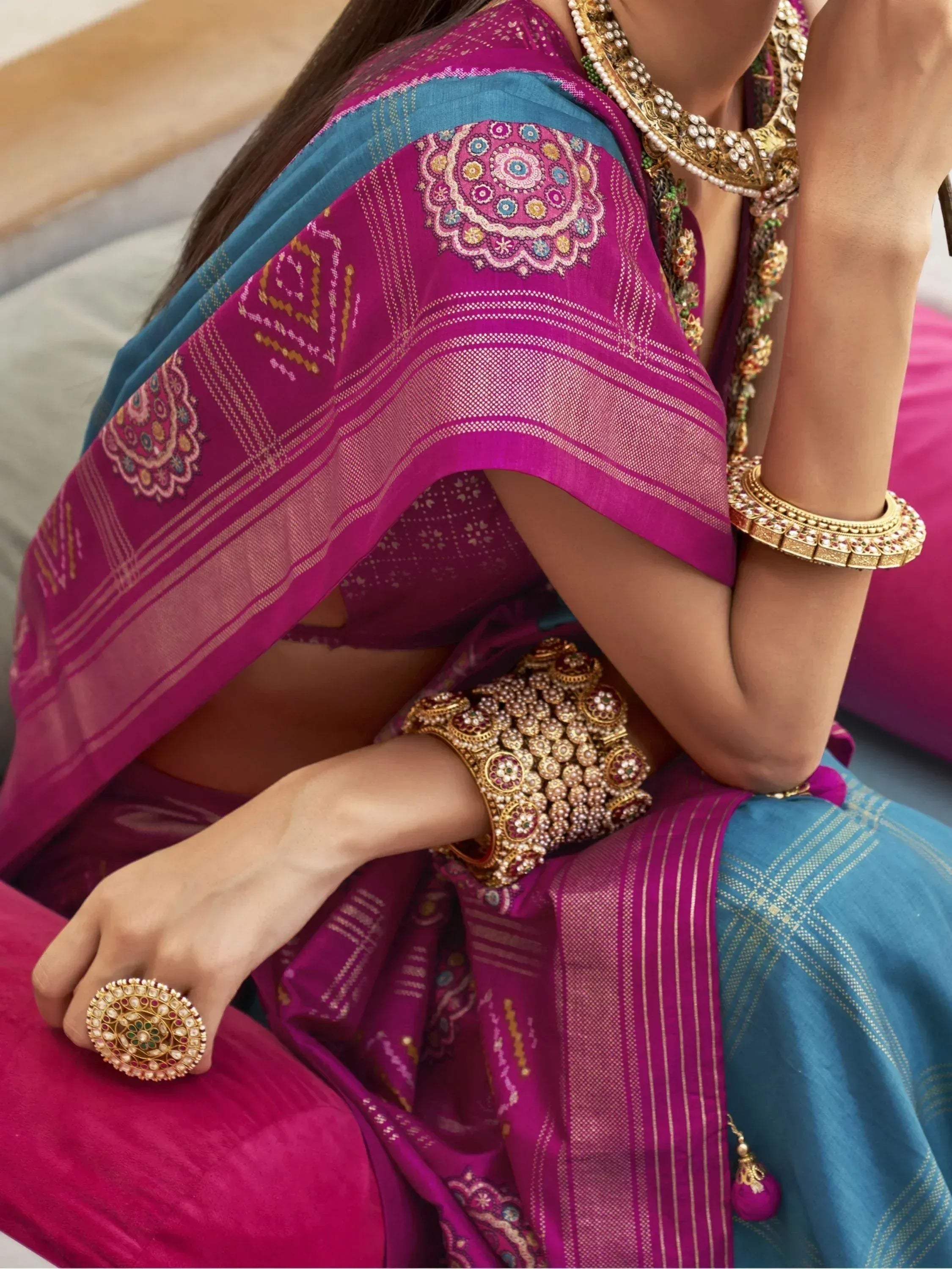 Woman in vibrant pink and blue ethnic saree with intricate embroidery and traditional gold jewelry