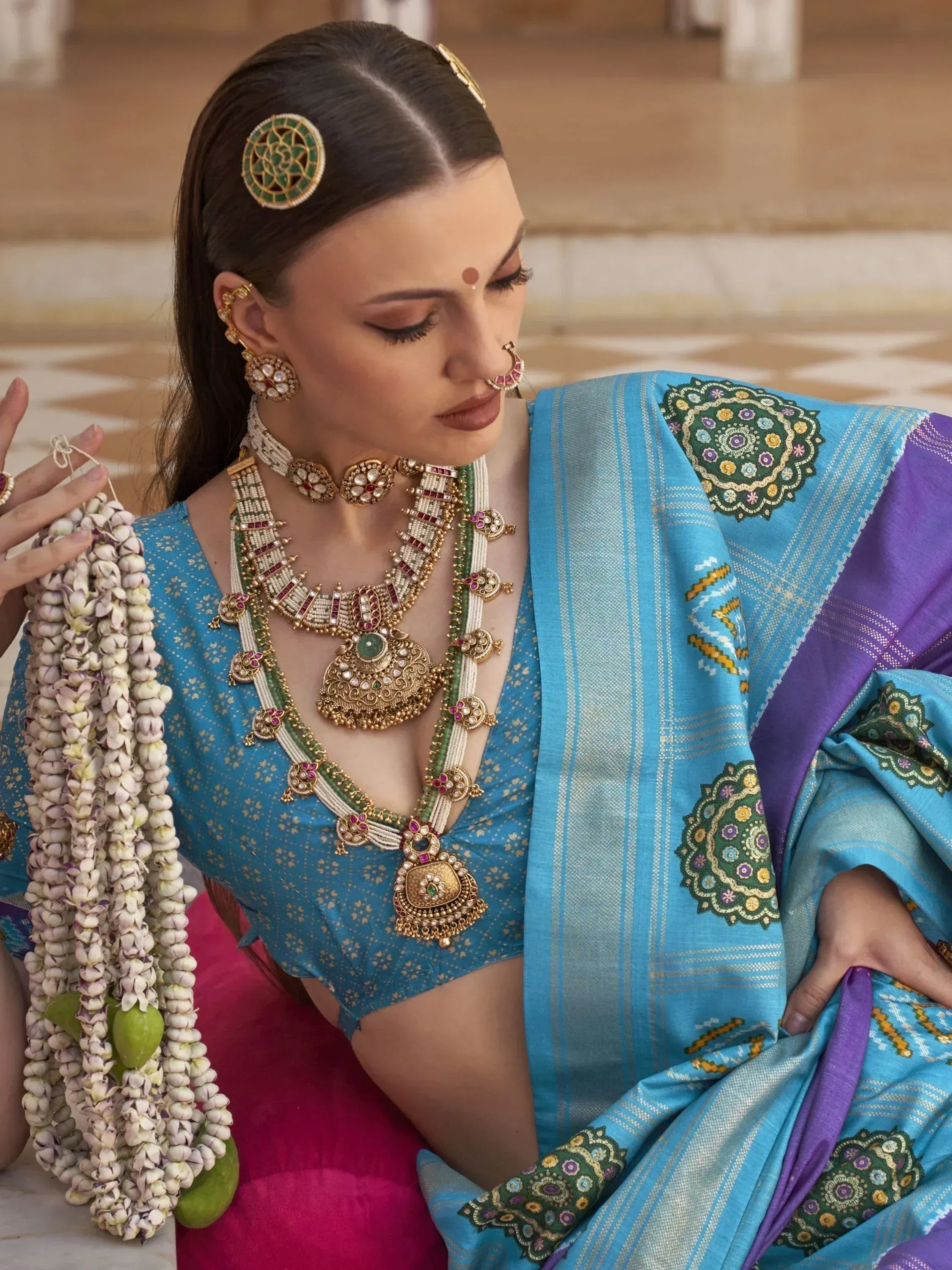 Woman in blue and purple ethnic saree with intricate jewelry and floral garland, traditional Indian attire